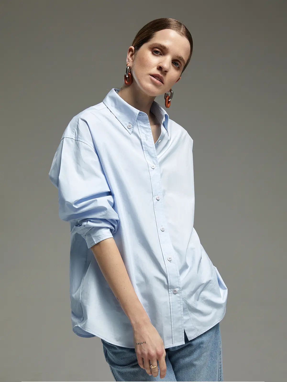 Front view of a model in a light blue oversized Pima cotton shirt with cuffed sleeves and visible button placket.