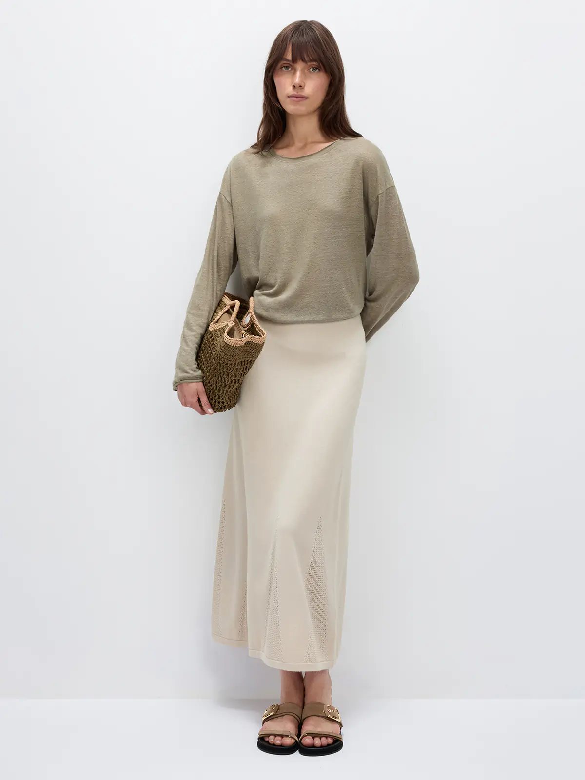 Front view of model wearing a grayish green lightweight long-sleeve linen t-shirt with relaxed drape, paired with a midi skirt and sandals.