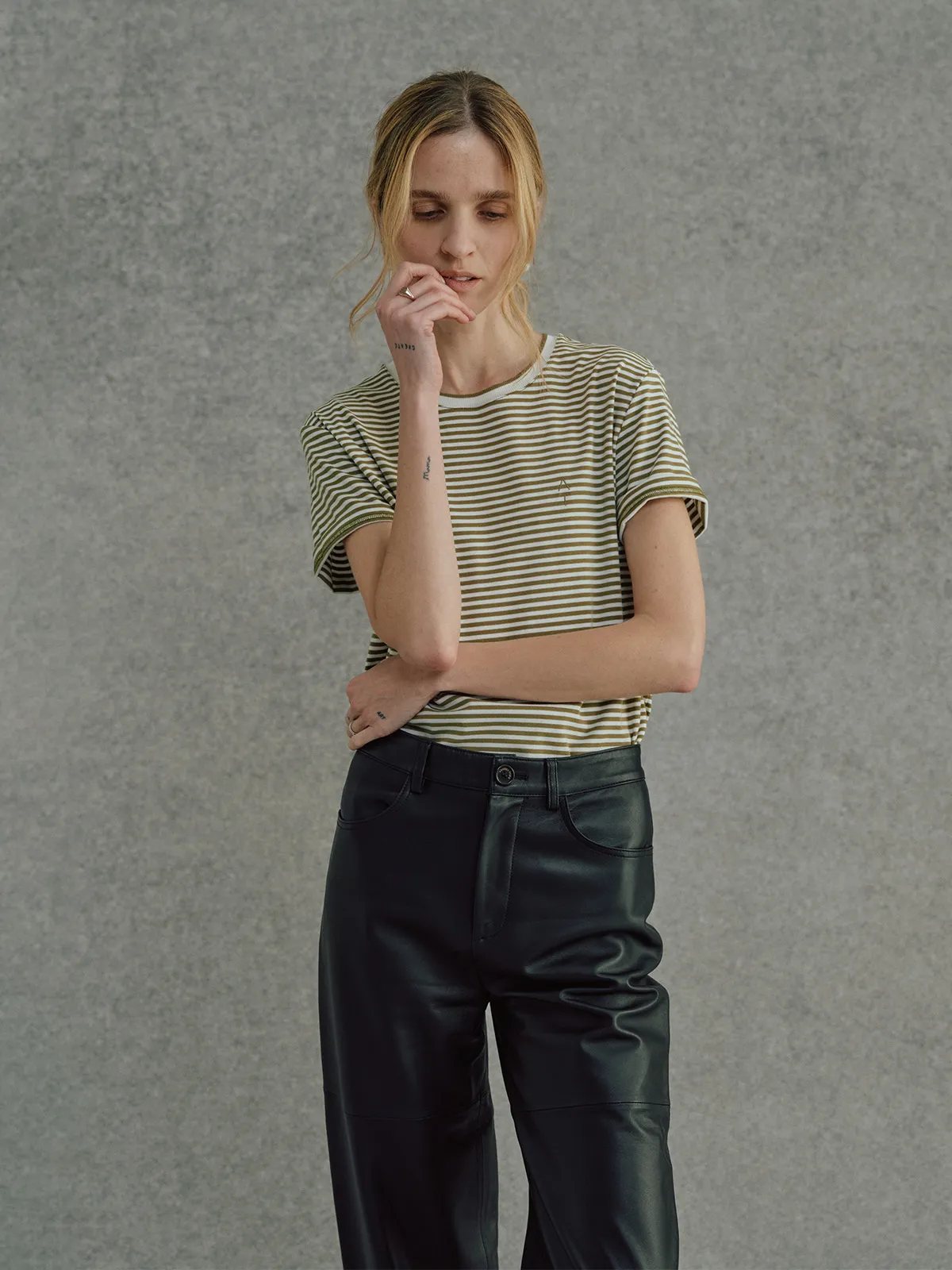 Model in FINLEY striped t-shirt with black leather trousers, side profile with hand near face, contemplative pose