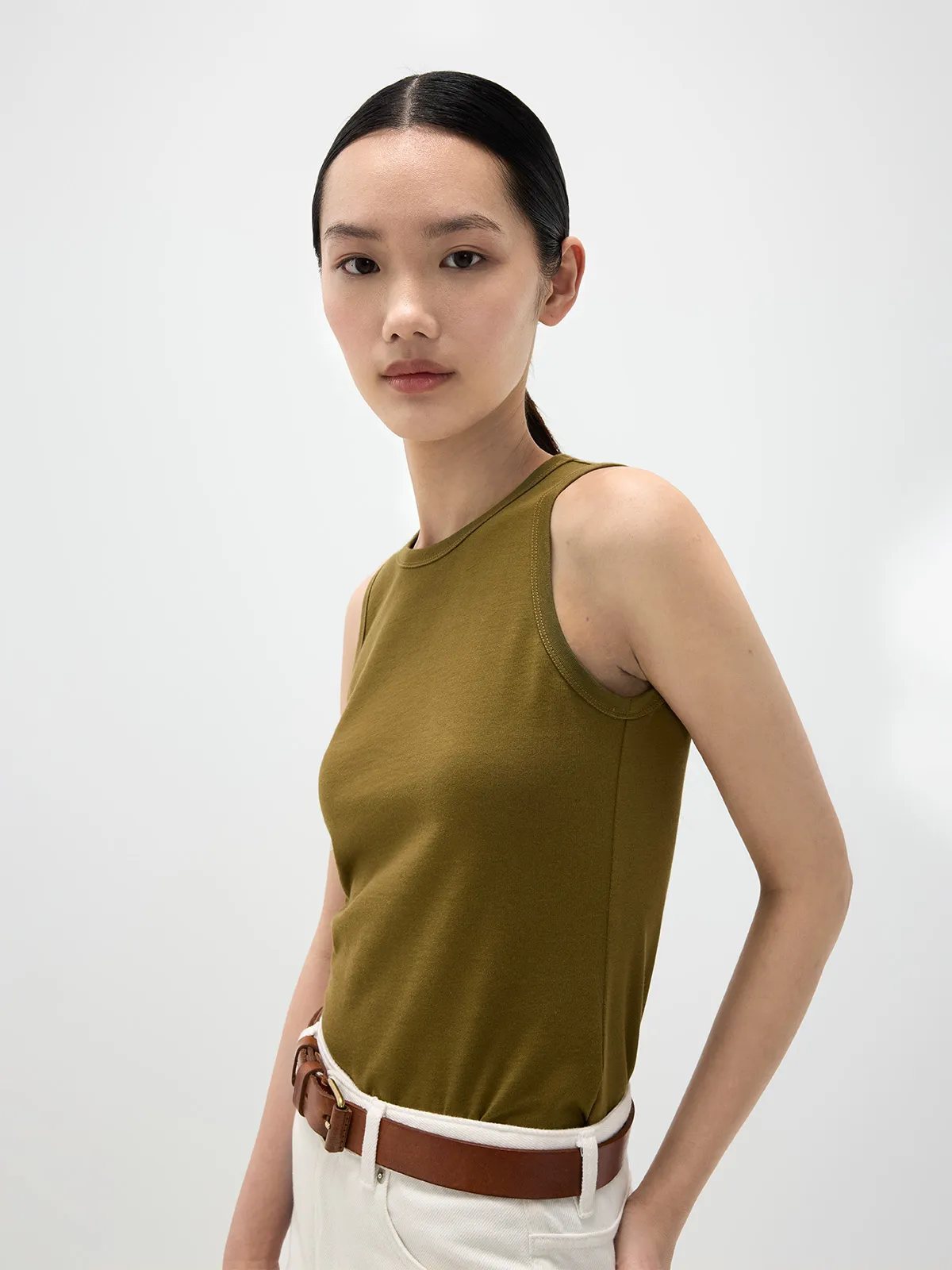 Asian model in olive HOLLY tank top with white denim trousers and brown leather belt