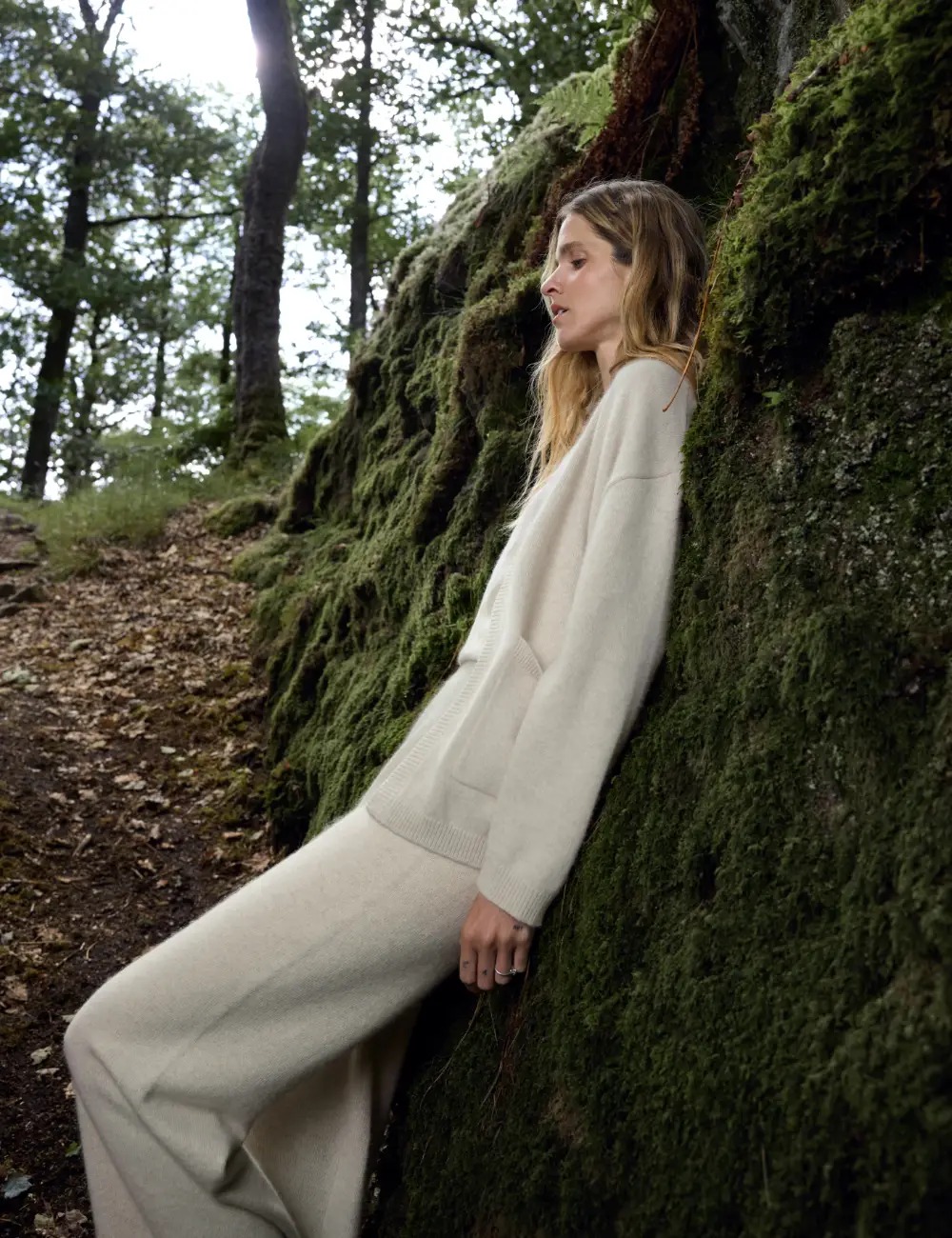 Woman in neutral knitwear standing beside a moss-covered tree