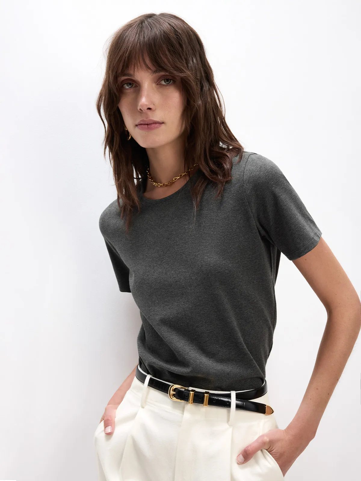 Model in charcoal SOSA t-shirt with white pleated trousers and gold chain necklace, minimalist chic