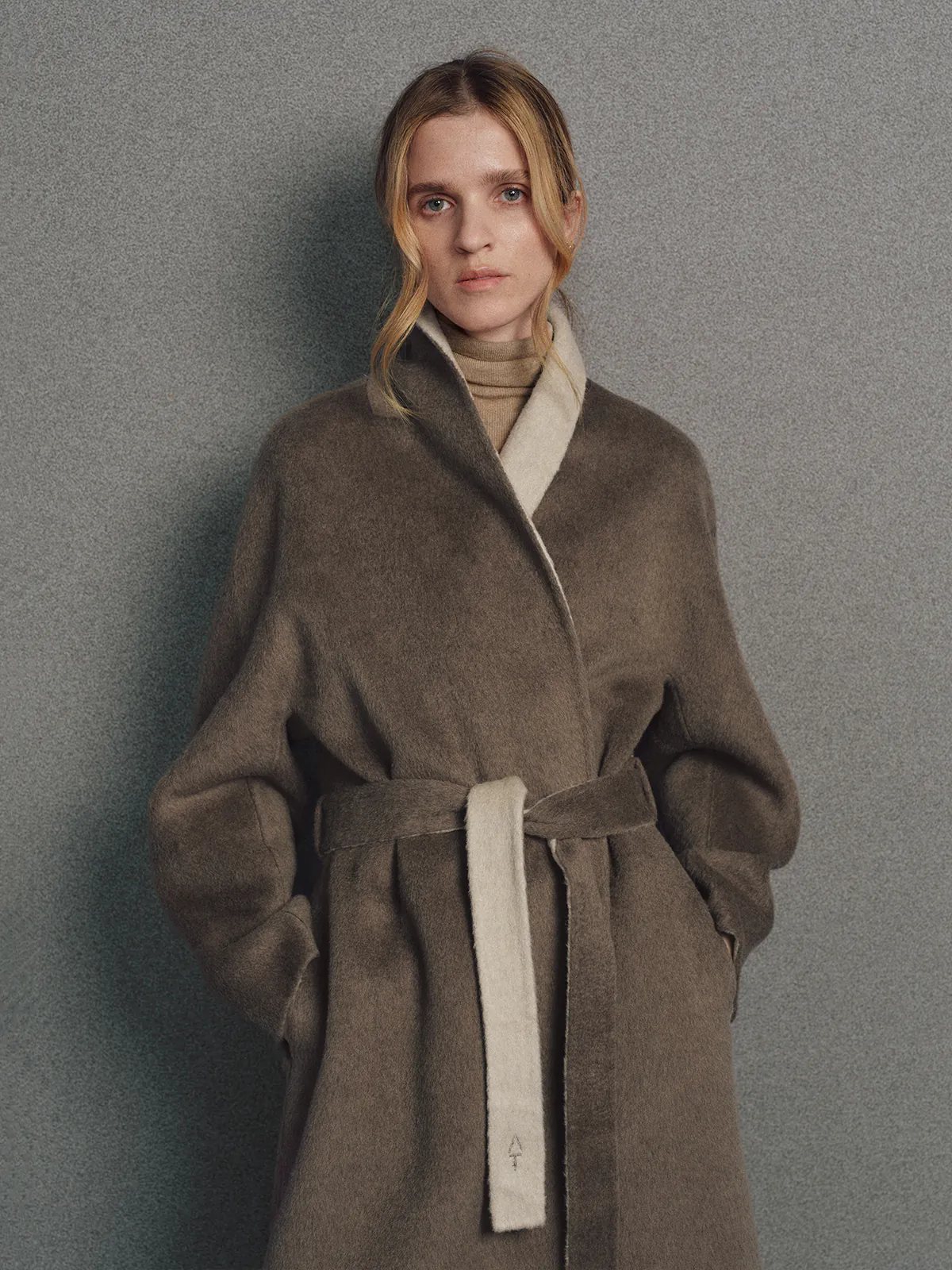 Front view of model in brown two-tone reversible notched-collar coat with lapel and tied belt.