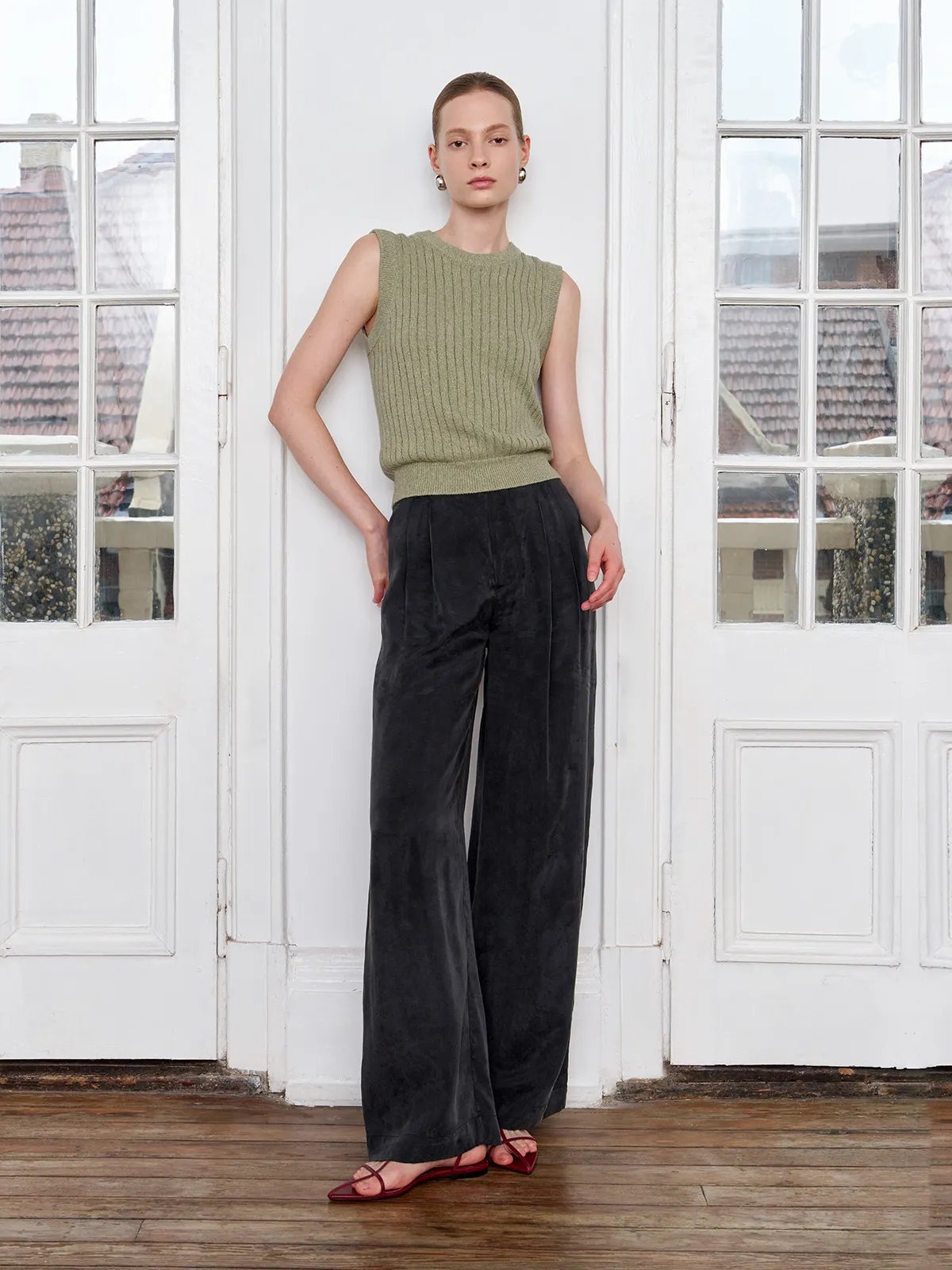 Andreatang MILLIE sleeveless knit tank top in sage green paired with black wide-leg corduroy trousers, model standing by white French doors — quiet luxury minimalist styling