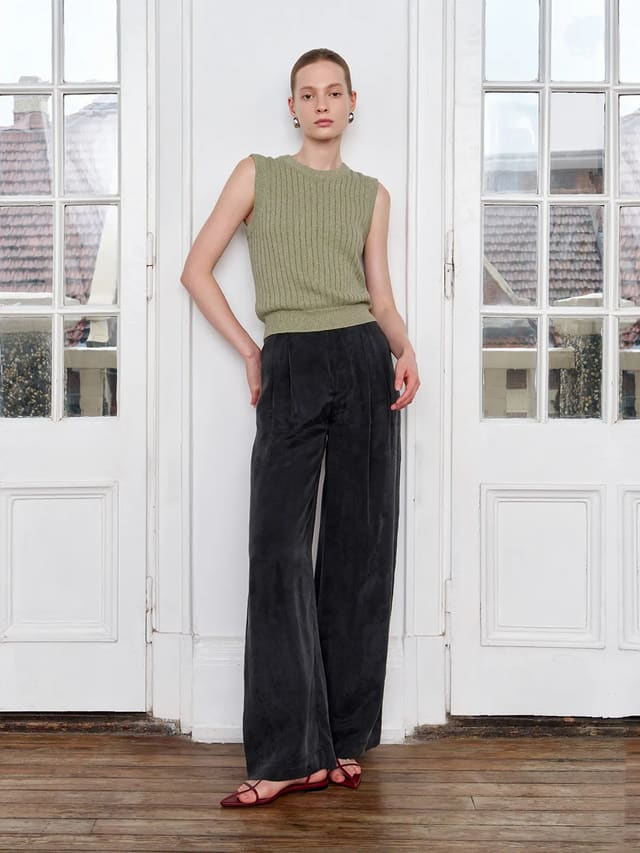 Andreatang MILLIE sleeveless knit tank top in sage green paired with black wide-leg corduroy trousers, model standing by white French doors — quiet luxury minimalist styling