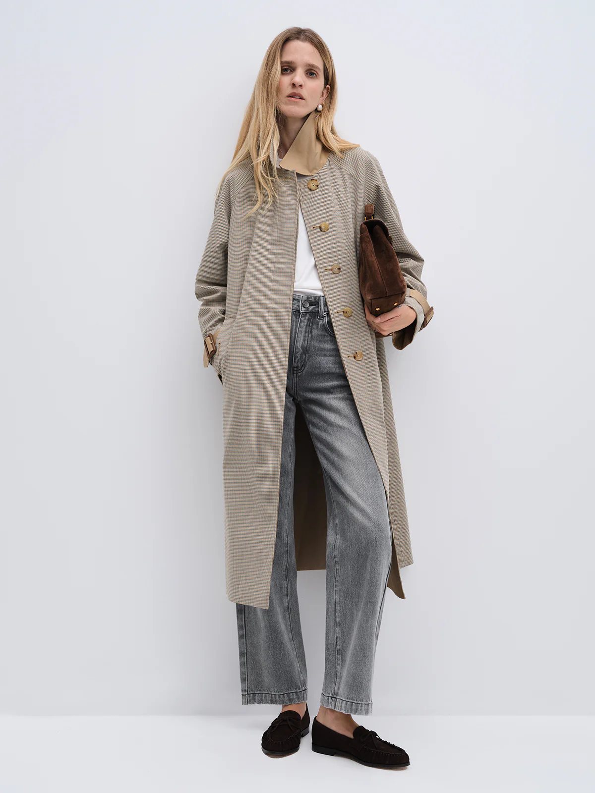Model in profile wearing a Khaki reversible check trench coat with visible inner lining, holding a clutch.