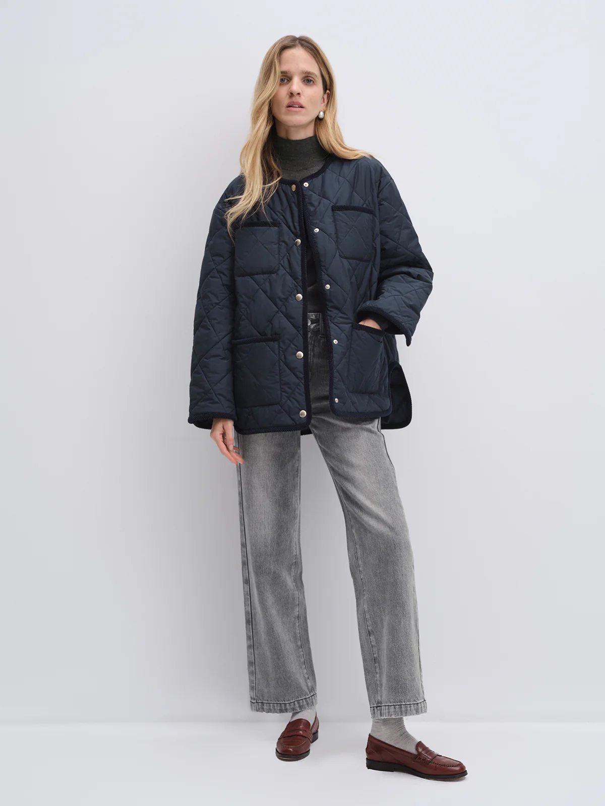 Model in navy quilted textured jacket with buttons and patch pockets, layered over dark turtleneck, hands in pockets.