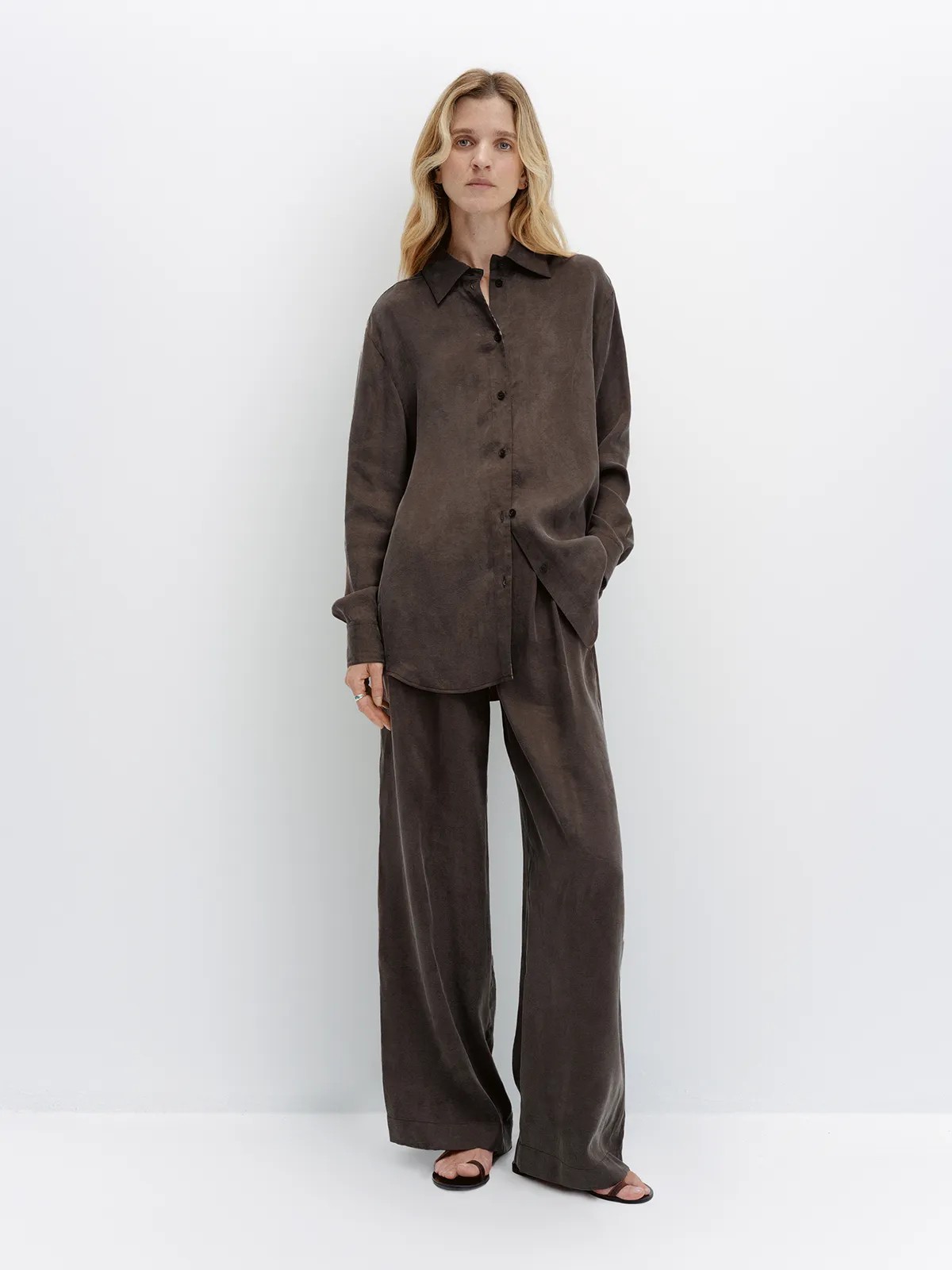 Full-length model in taupe NOBU Shirt and trousers with flat sandals, standing against white backdrop