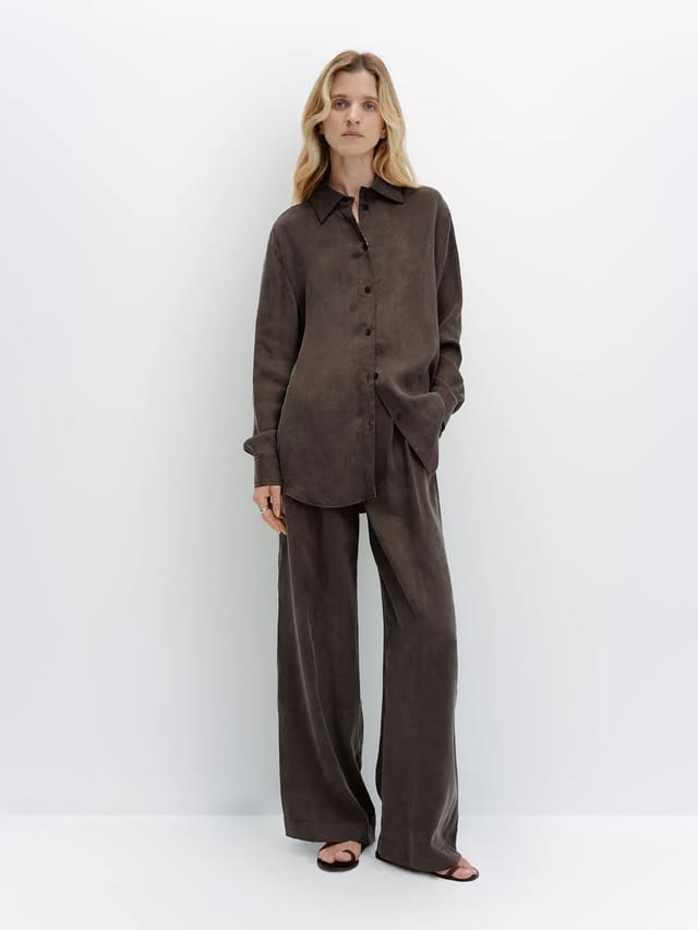 Full-length model in taupe NOBU Shirt and trousers with flat sandals, standing against white backdrop