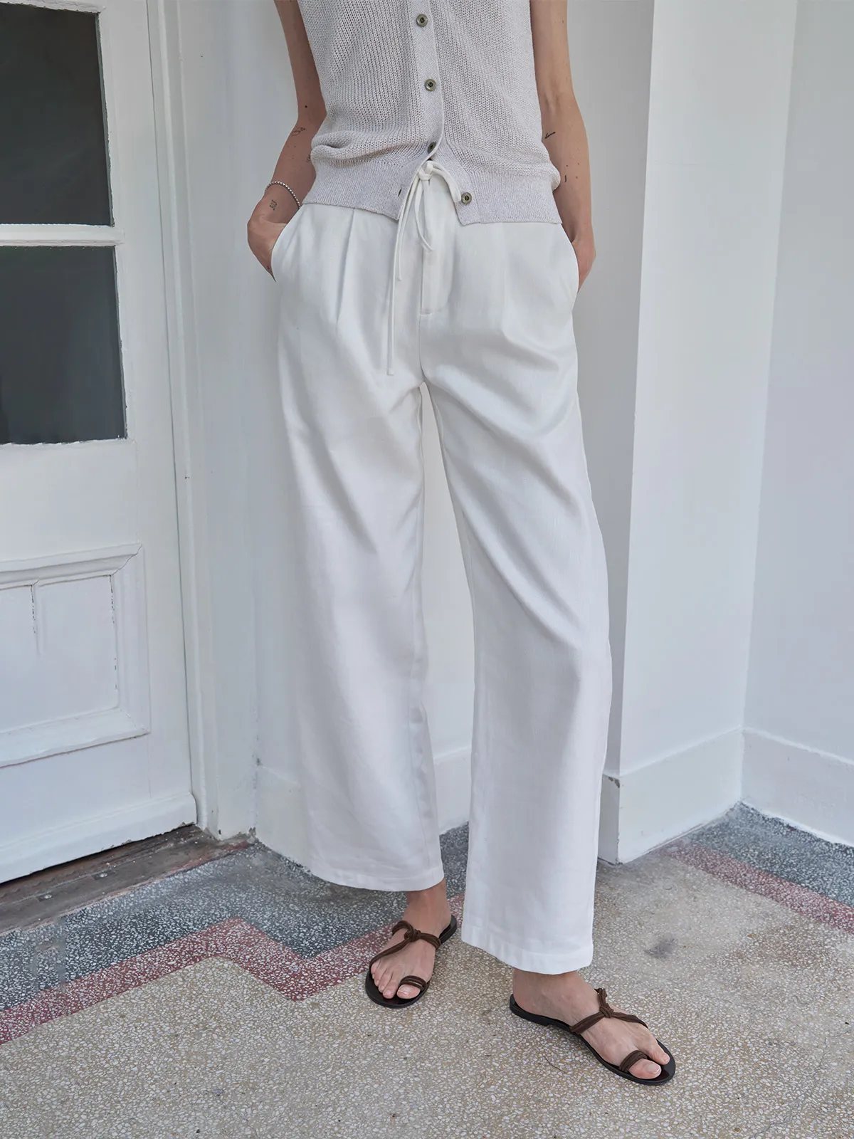 Mid-shot of model hands in pockets, highlighting front pocket placement and relaxed fit of white LEIGHTON trousers