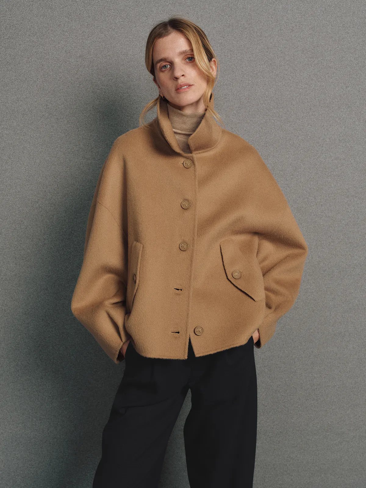 Model in the Camel KELSEY short jacket with notched collar, four front buttons, and flap pockets, styled with trousers and turtleneck.