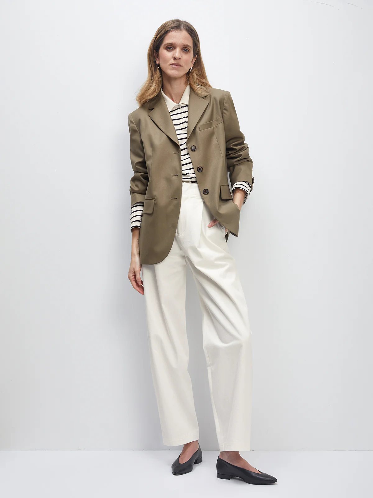 Model in the Black Wool Acetate Cuban-Collar Blazer with a buckle belt, striped top, and trousers.