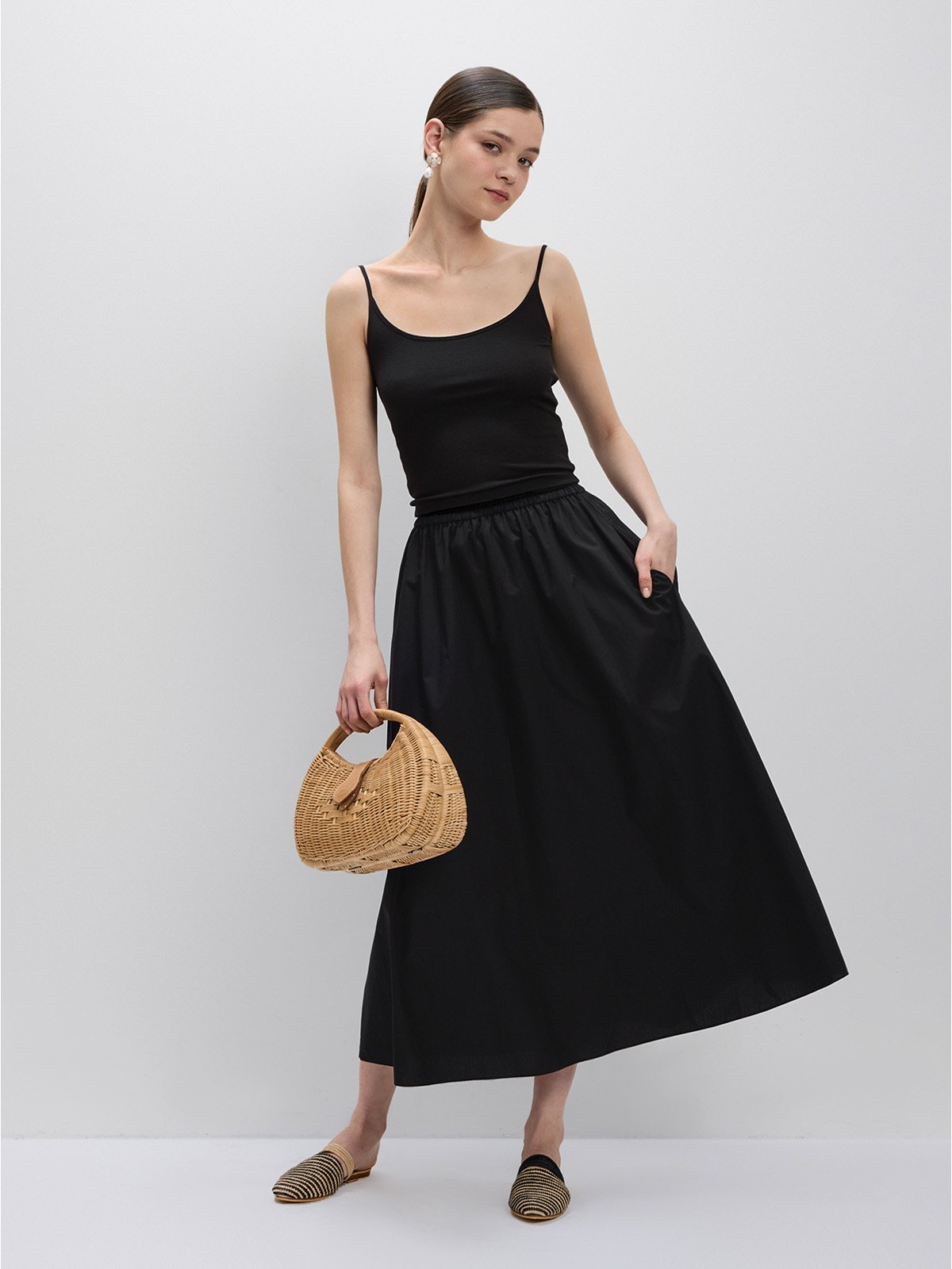 Black Lyocell cotton A-line maxi skirt with black tank, woven straw bag, and striped loafers, full-body studio pose