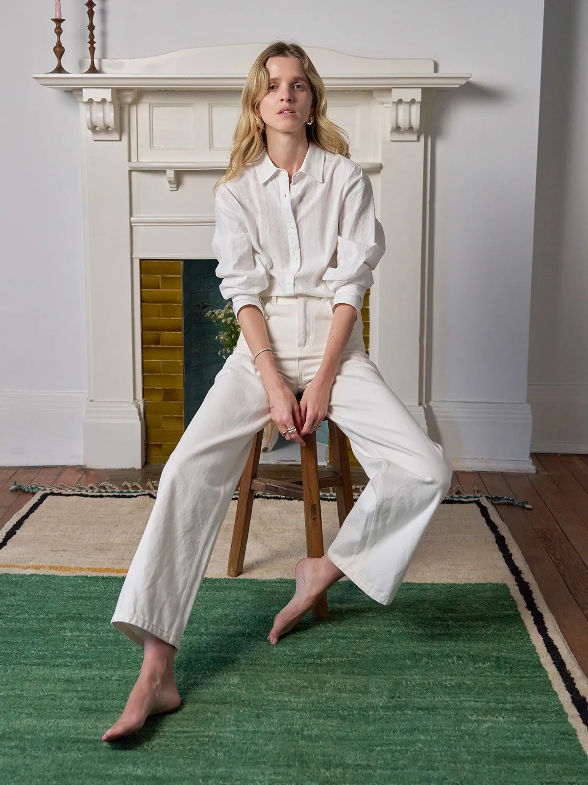 Model seated on wooden stool wearing RORY shirt with wide-leg white trousers