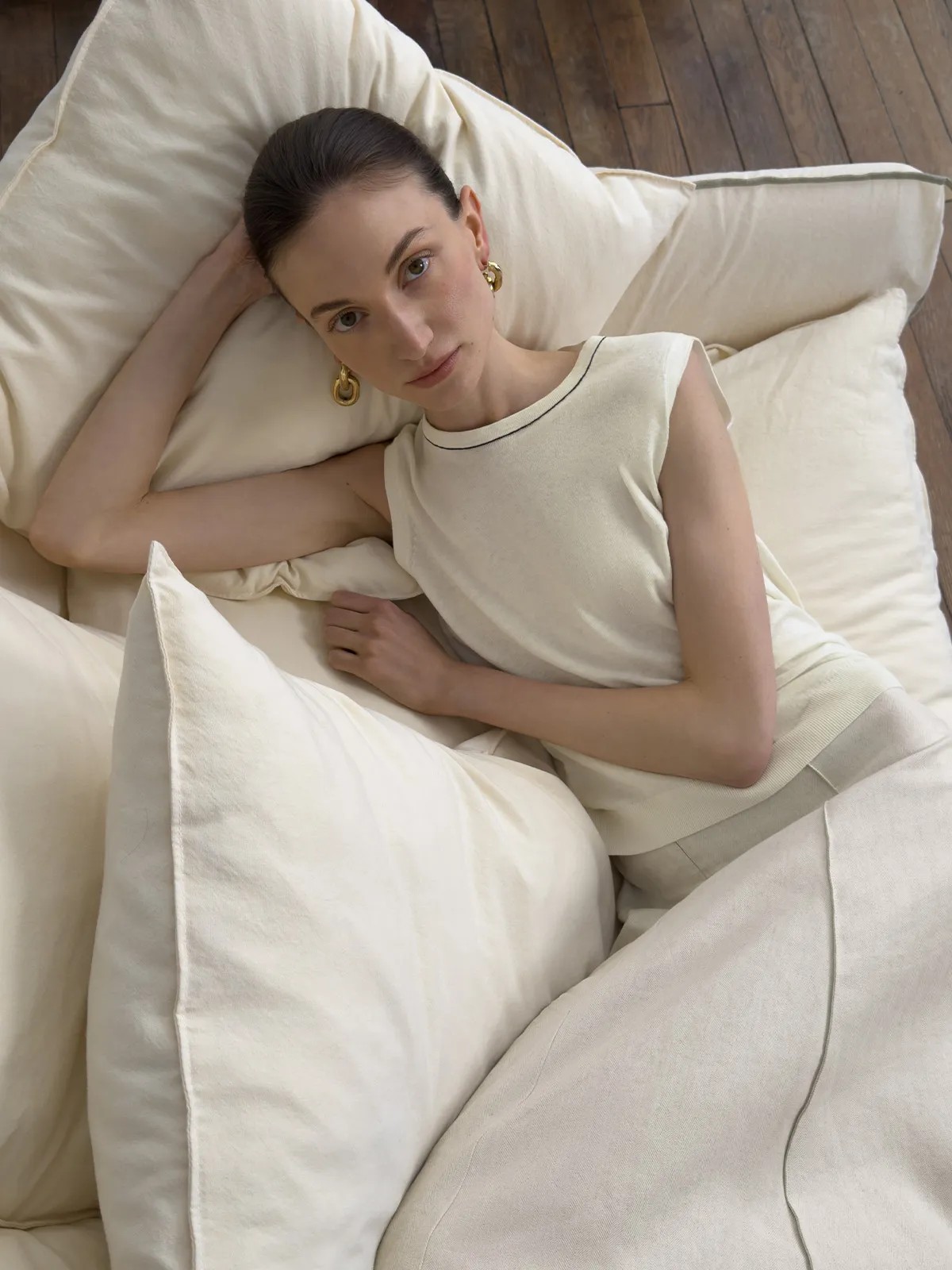 Model reclining on ivory pillows wearing sleeveless knit top, conveying relaxed sophistication