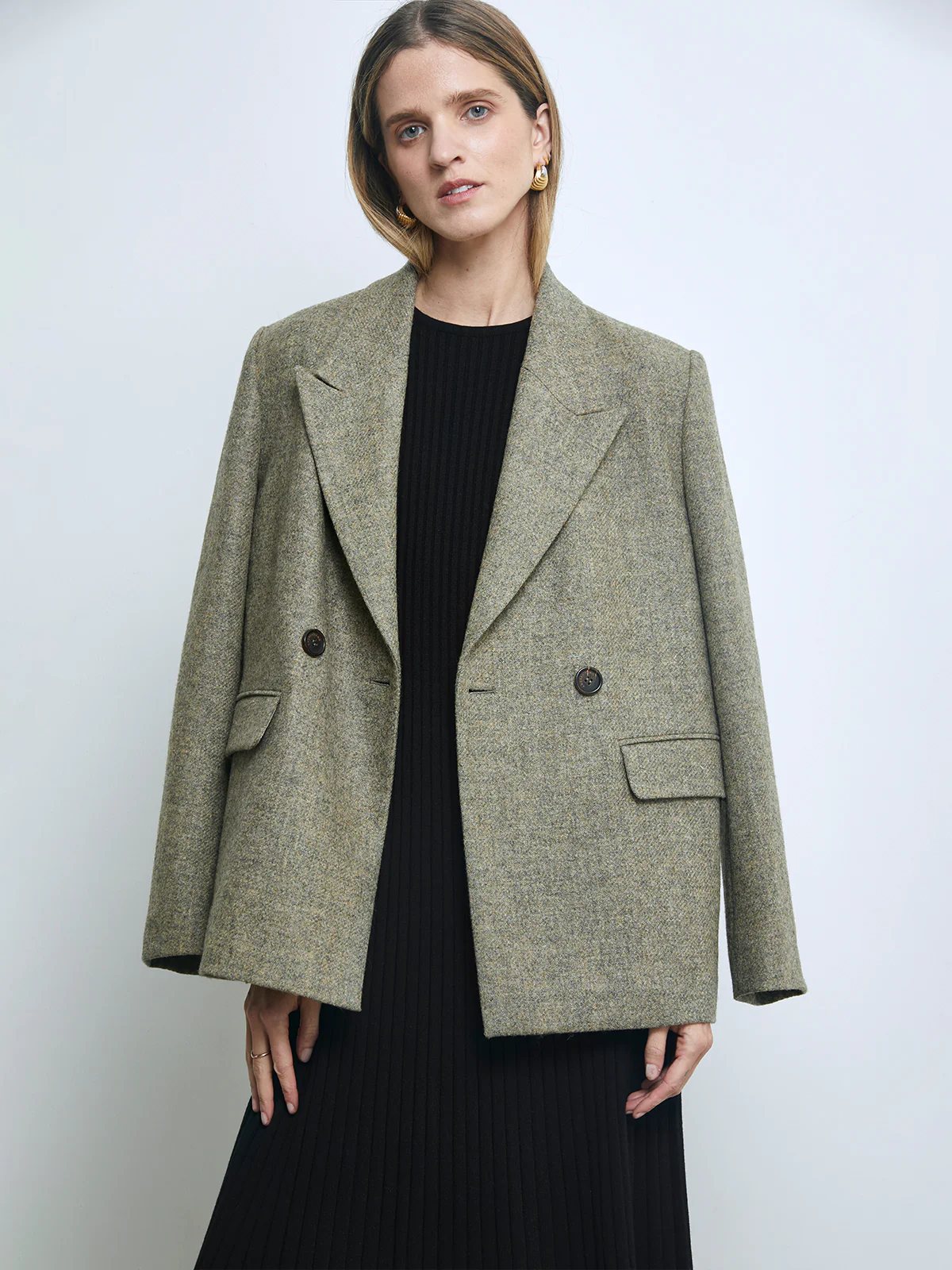 Front view of a model in a Sage Green pure wool tweed double-breasted blazer over a ribbed dress, hands at sides.