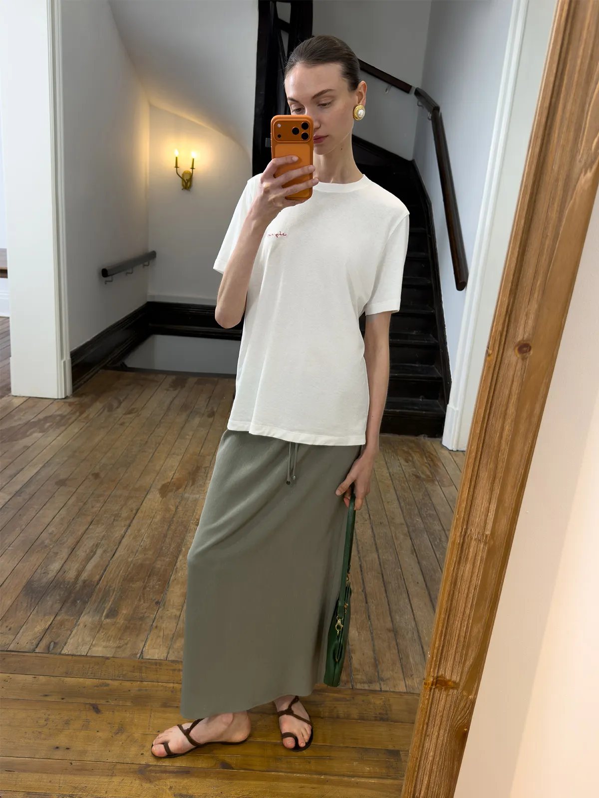 Mirror selfie of model in KATRINA skirt with white embroidered tee and green shoulder bag