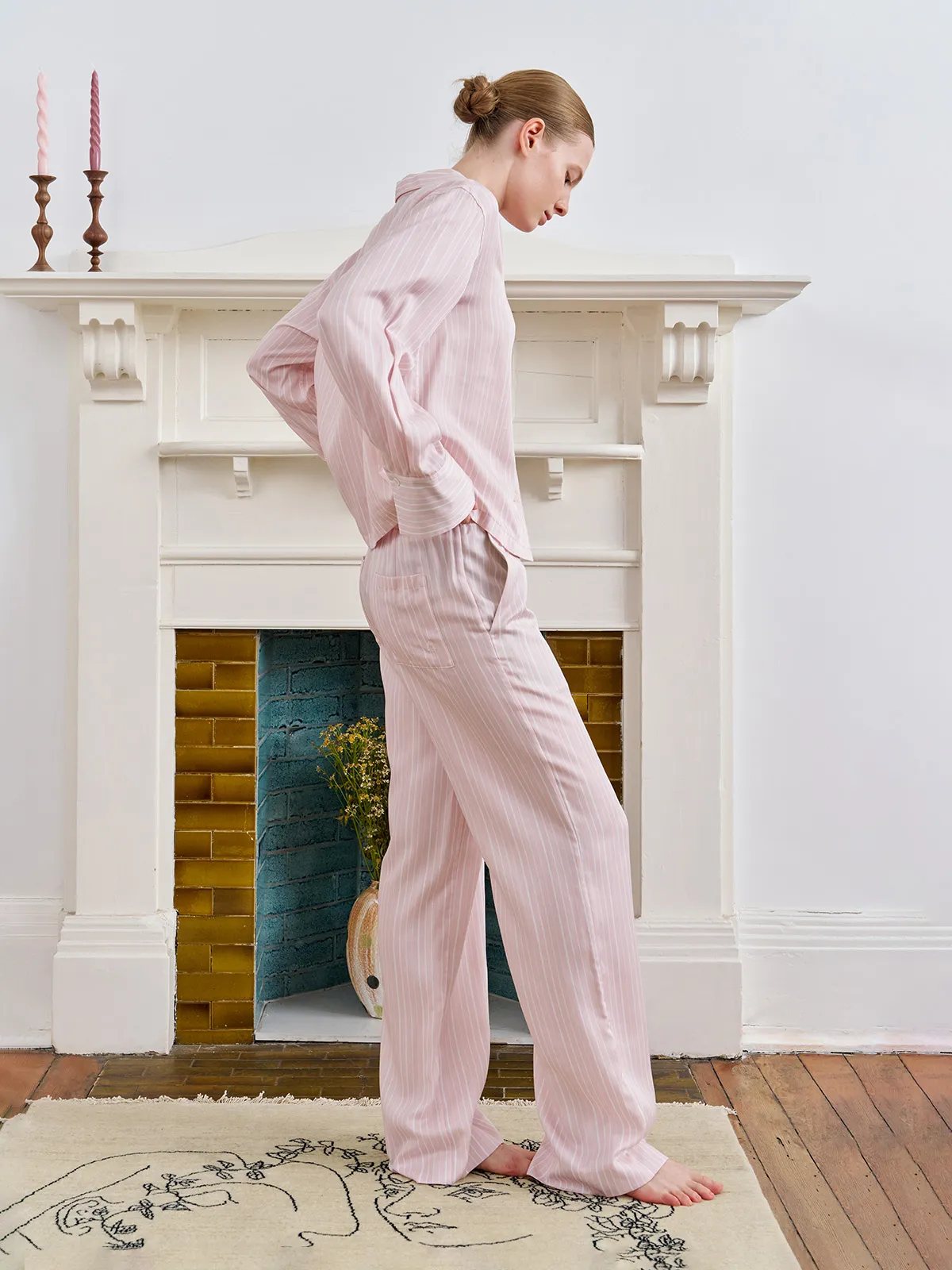 Model standing in profile wearing LARISSA pajama set, hands in pockets, white fireplace backdrop