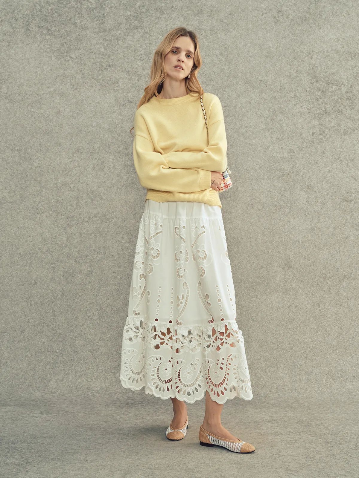 Model in lemon JILL jumper with arms crossed, paired with white embroidered lace midi skirt and woven flats