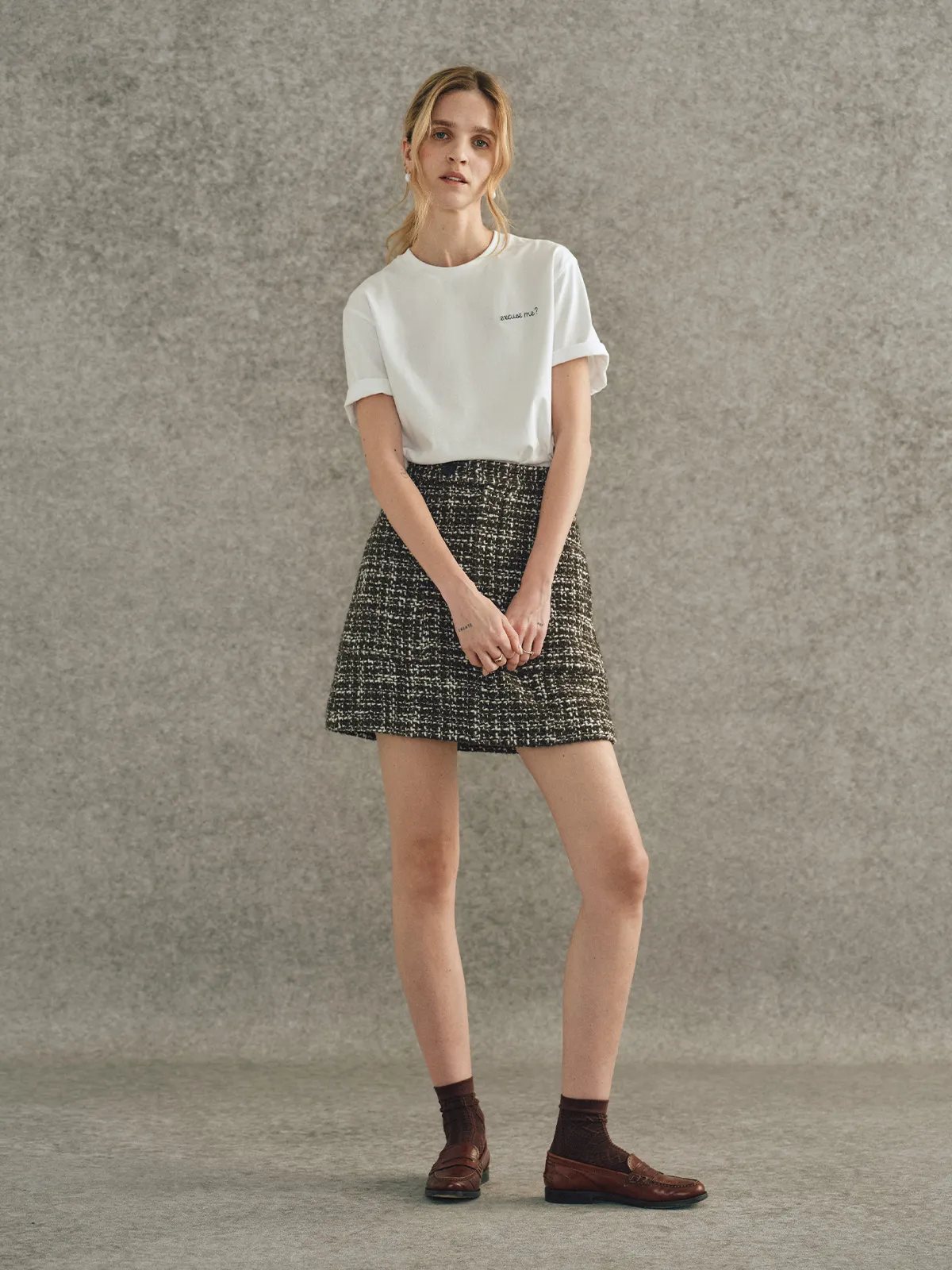 Model in white embroidered t-shirt with tweed mini skirt, brown loafers, and socks