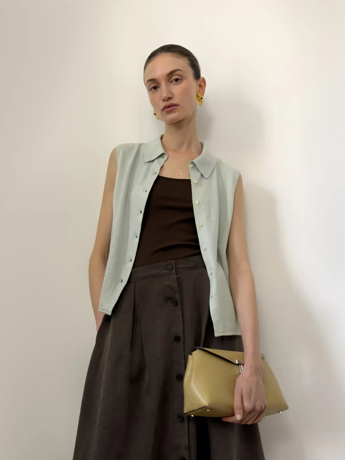 Model wearing MARGOT sleeveless knit shirt layered over brown ribbed tank with brown skirt and gold earrings