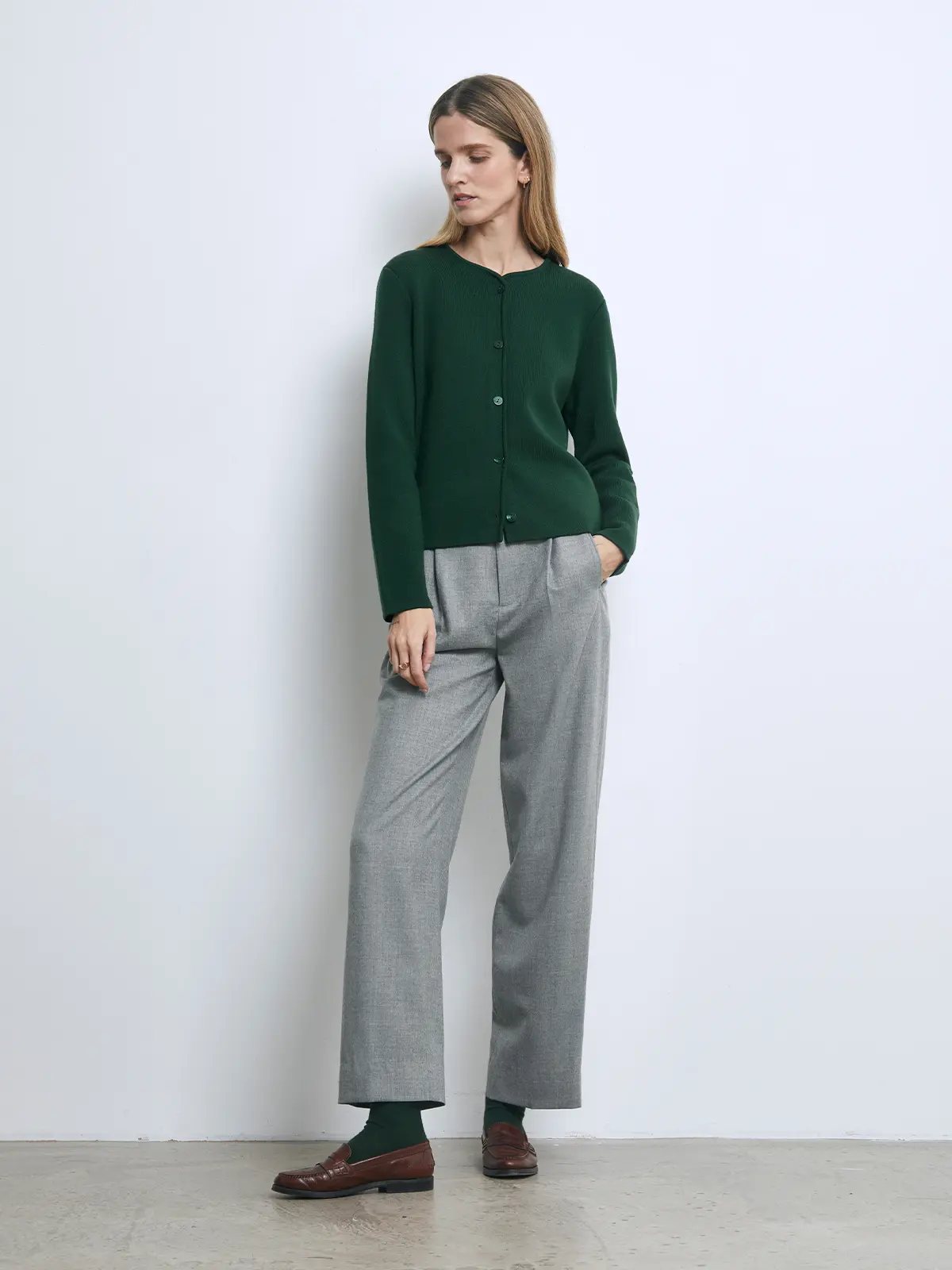Front view of a model wearing a green knit cardigan layered over a dark turtleneck with wide-leg jeans and mesh flats.