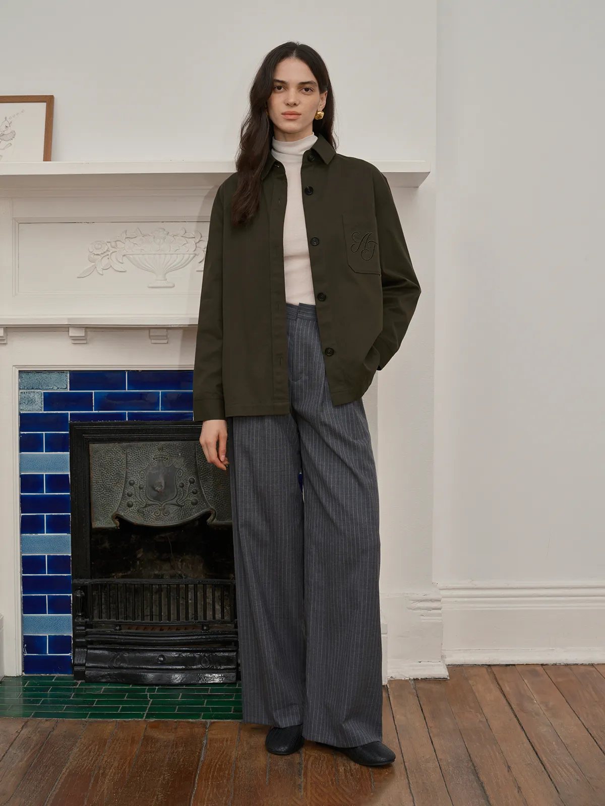 Front full-length view of model in HUCK jacket, white turtleneck, wide-leg pinstripe trousers, black loafers