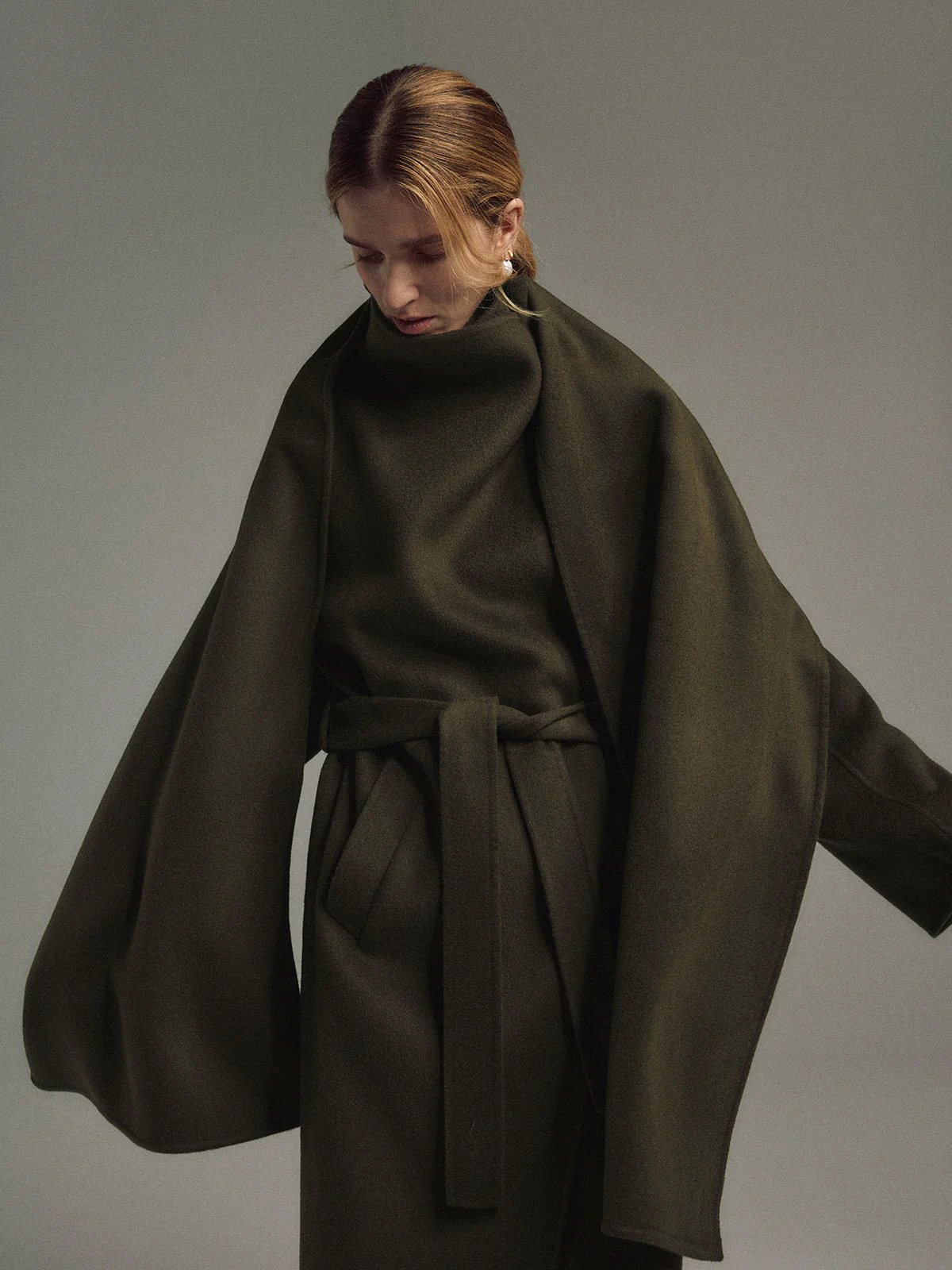 Side view of the Olive TANSY long coat worn open with a self-fabric belt tied at the waist, showing drape and volume.
