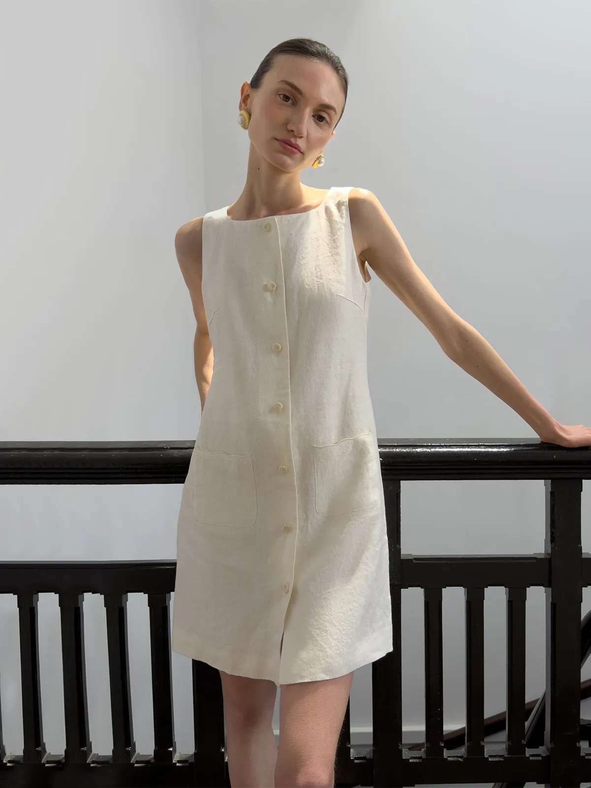 Model in ivory MARISA dress side pose leaning on black railing