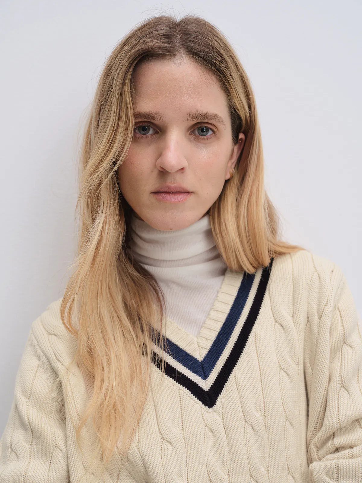 Off-white cable knit V-neck tennis jumper with contrasting trim, shown in a close-up front view over a turtleneck.
