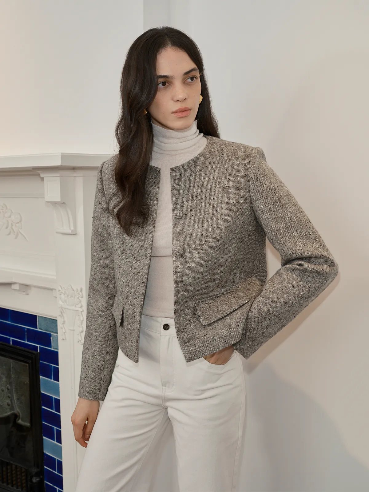 CLARKE Boxy Tweed Jacket styled with white wide-leg trousers and cream turtleneck—modern minimalist look by fireplace