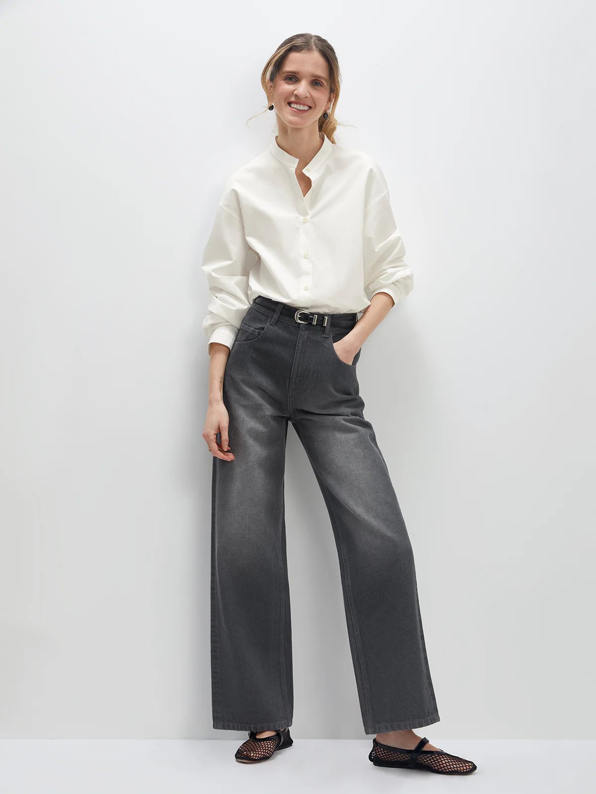 Front view of model wearing gray wide-leg jeans with button-up shirt, belt, and mesh flats.