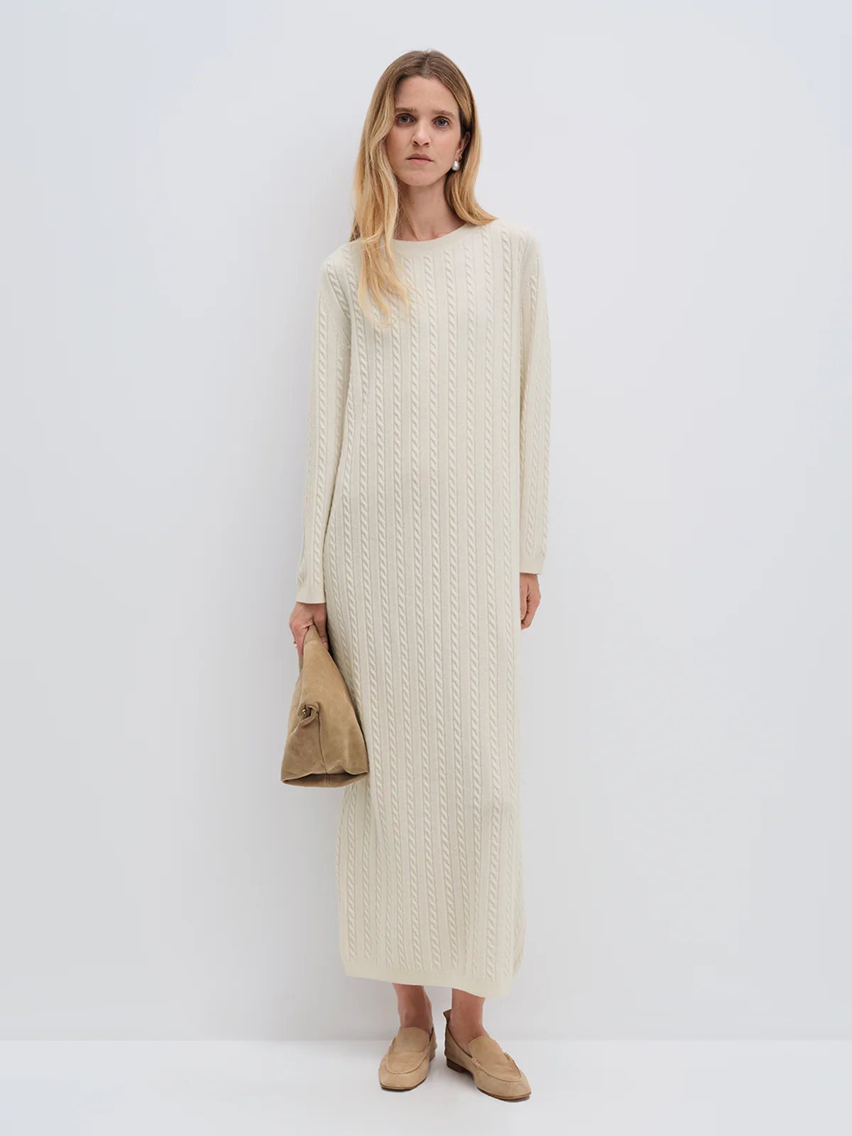 Model wearing andreatang cream Merino wool cable-knit maxi dress with raglan sleeves, styled with tan loafers and clutch