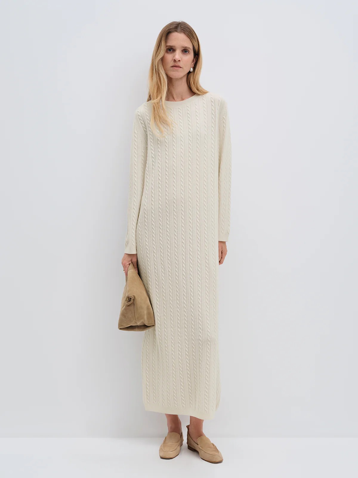 Model wearing andreatang cream Merino wool cable-knit maxi dress with raglan sleeves, styled with tan loafers and clutch