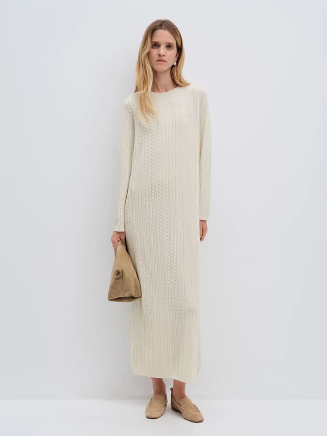 Model wearing andreatang cream Merino wool cable-knit maxi dress with raglan sleeves, styled with tan loafers and clutch