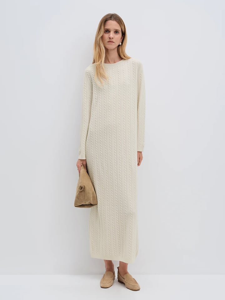 Model wearing andreatang cream Merino wool cable-knit maxi dress with raglan sleeves, styled with tan loafers and clutch
