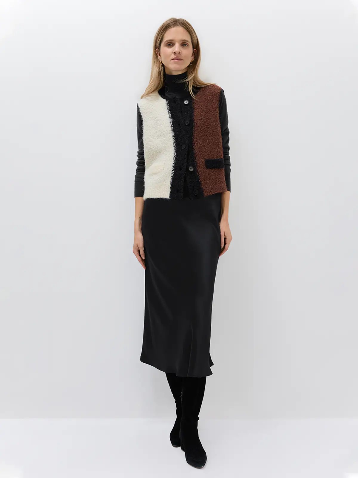 Model poses front-on wearing the Brown/White/Black colorblock knitted vest over a white blouse and black trousers, hands in pockets.