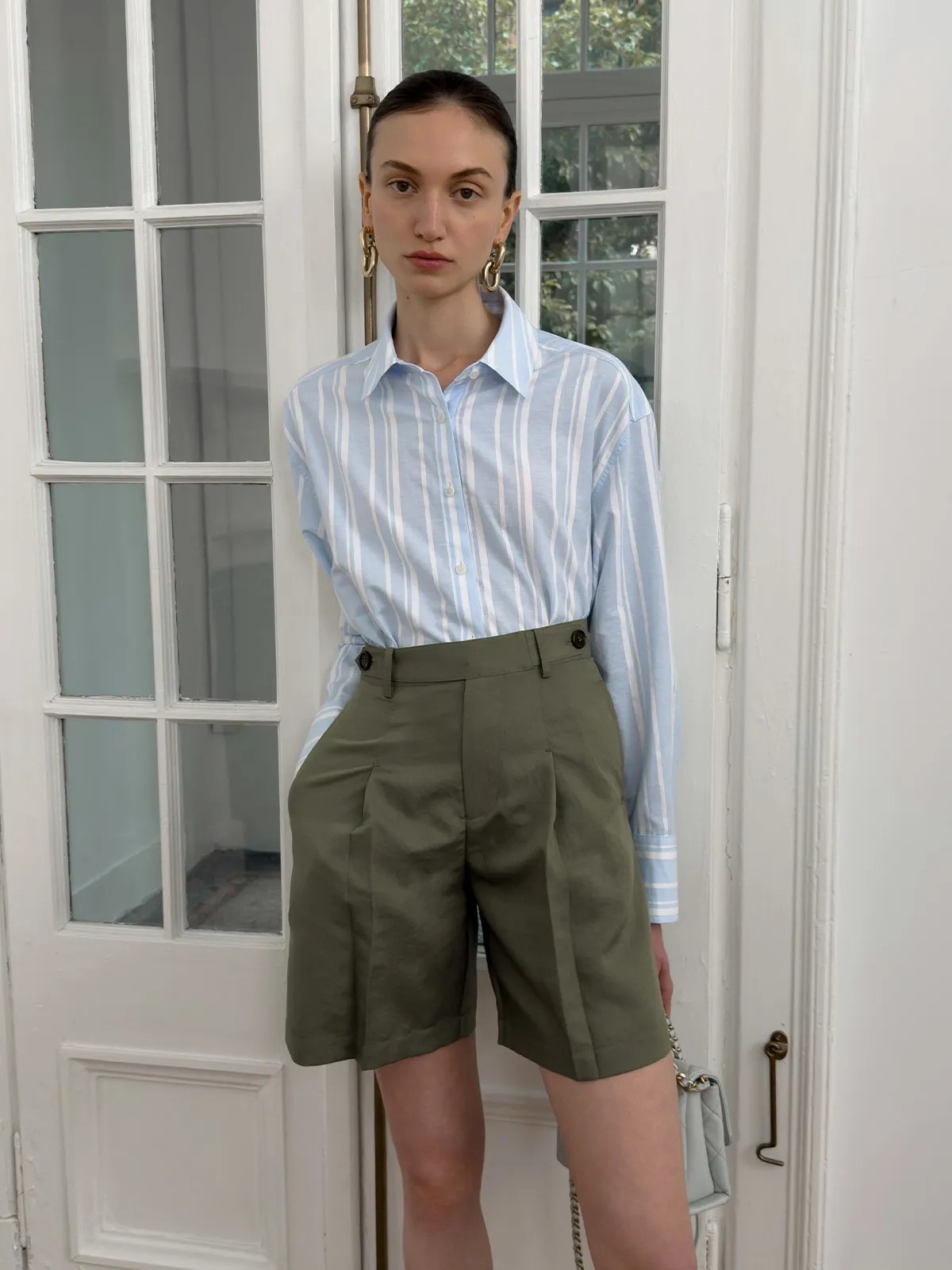 Model in olive green ADELE Bermuda shorts with striped blue-white shirt and light grey bag