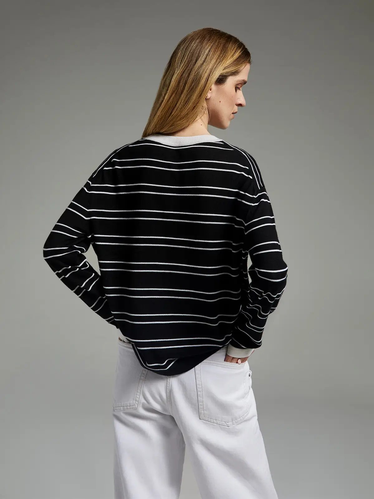 Back view of model wearing a black knit top with horizontal stripes and pants.