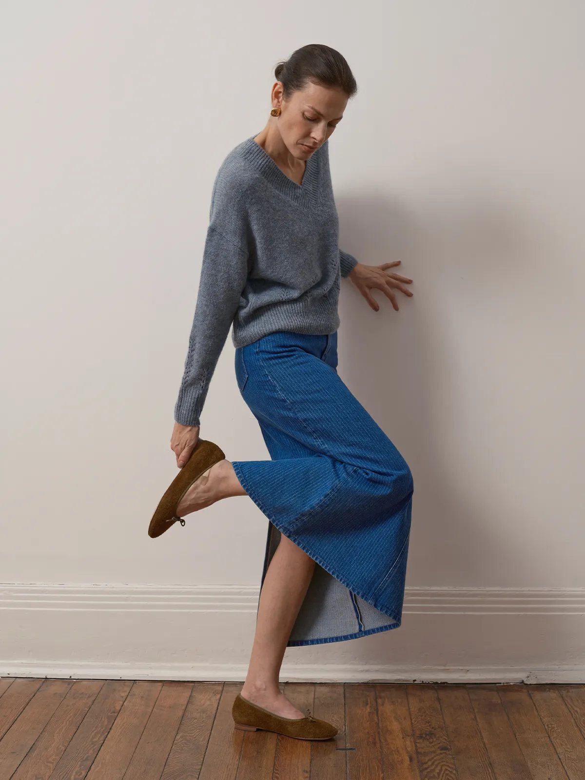 Dynamic pose: model lifting leg to reveal BRYCE skirt’s side slit and layered hem detail with gray V-neck sweater