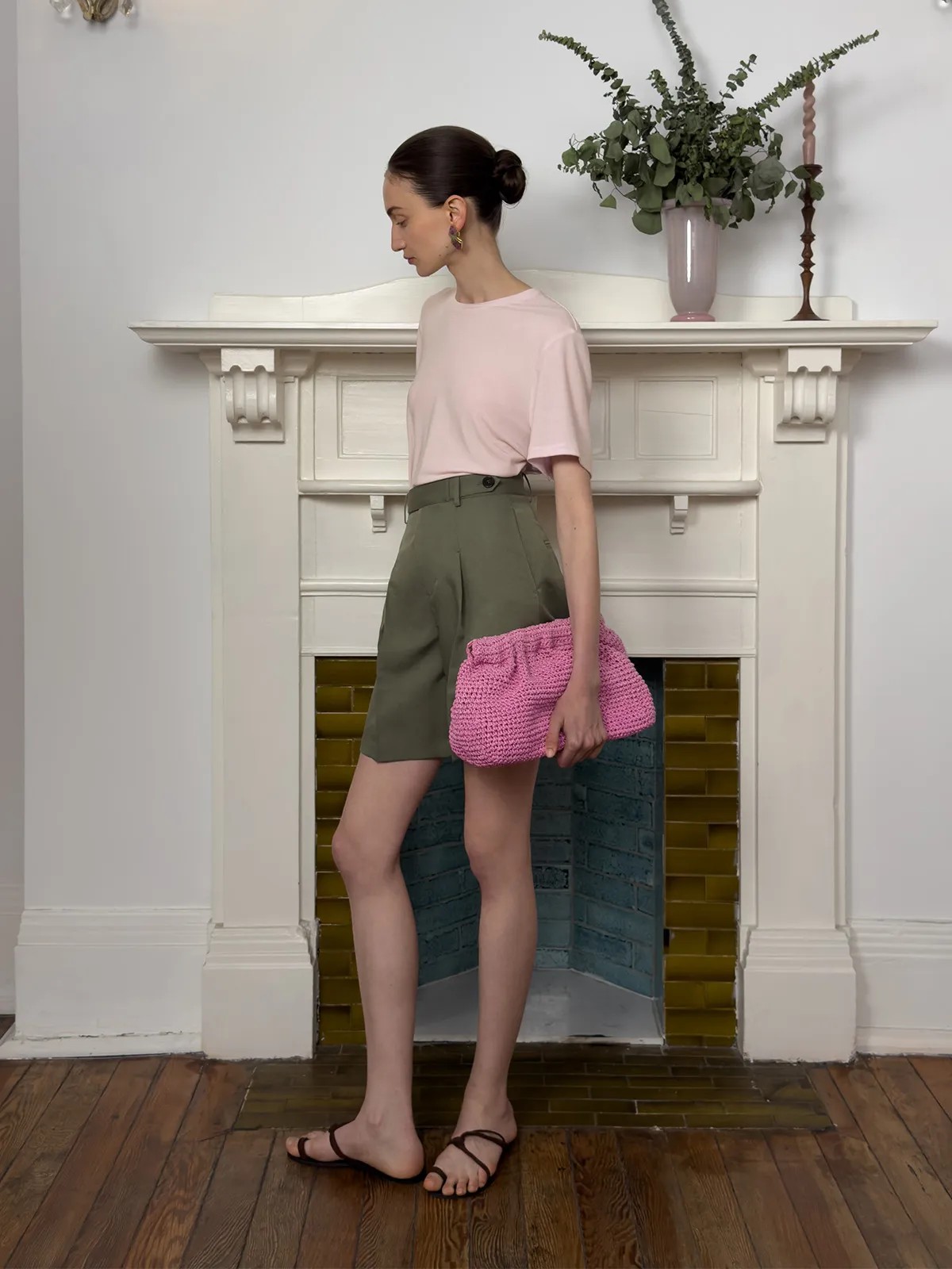 Side profile of model in blush MARY T-Shirt, olive green tailored shorts, and pink crocheted clutch—quiet luxury summer styling