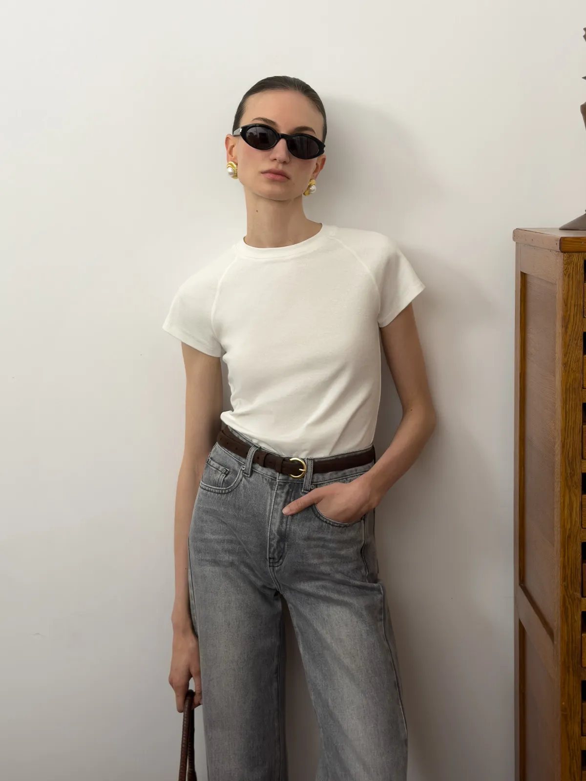 Front view of andreatang LUCA white fitted raglan t-shirt with cap sleeves, worn with grey jeans and gold belt