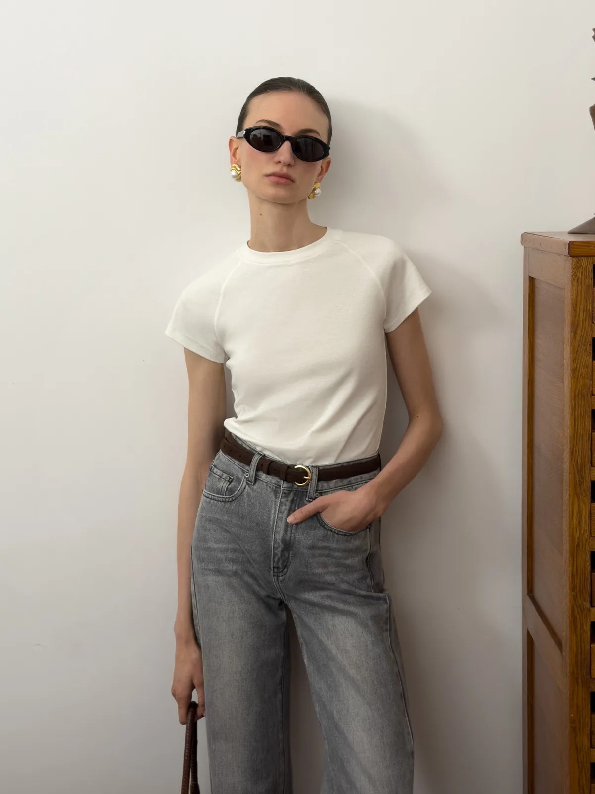 Front view of andreatang LUCA white fitted raglan t-shirt with cap sleeves, worn with grey jeans and gold belt