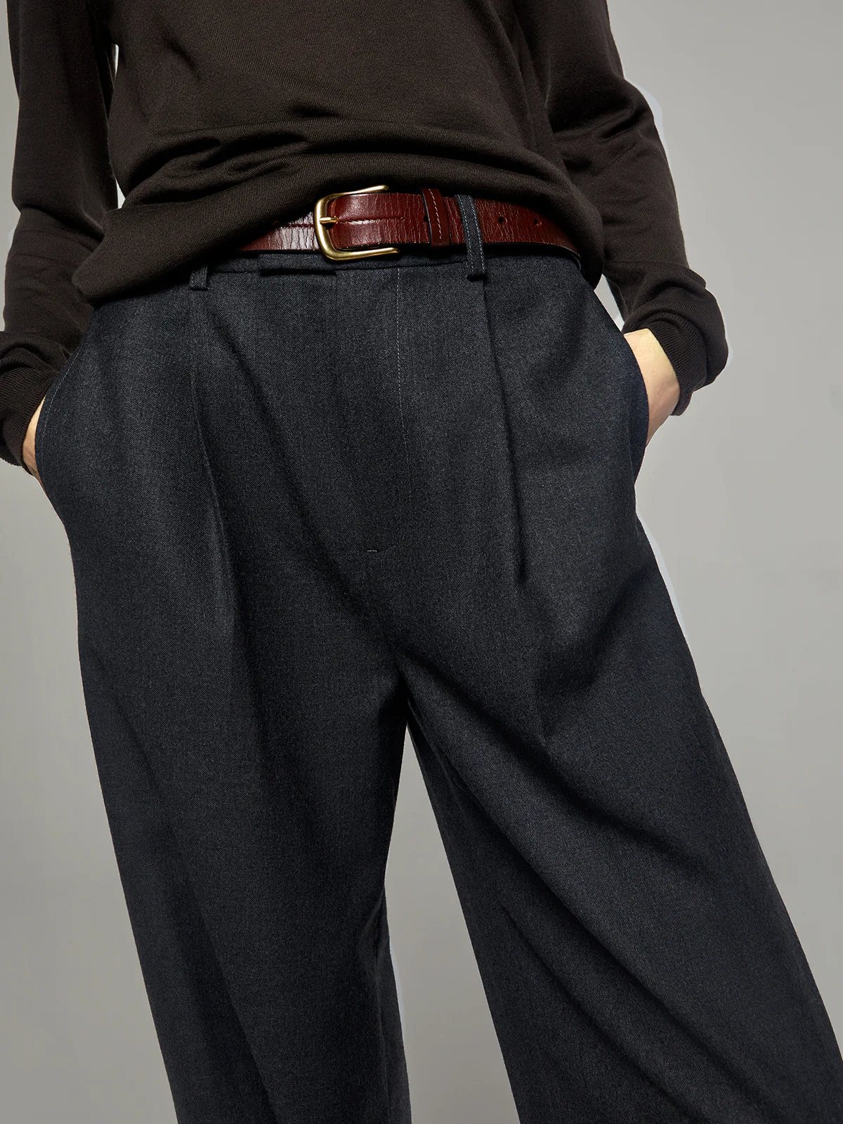 Side view highlighting drape and wide leg of Gray fine wool trousers, worn with dark top and belt.