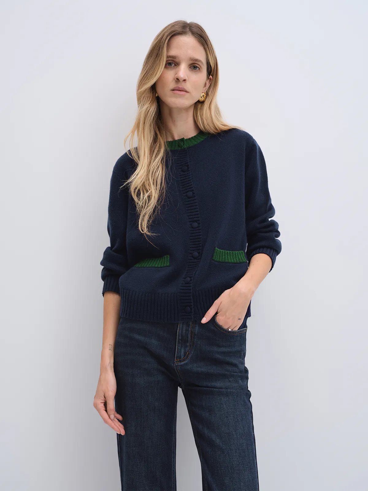 Model in navy cardigan with contrast trim at collar and patch pockets, hands in jeans pockets, front-facing pose.