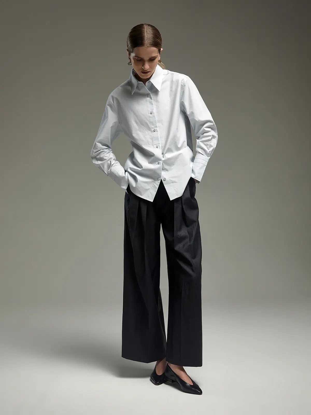 Pale Blue paper-texture cotton shirt with classic collar, worn untucked over wide-leg trousers, model looking down.