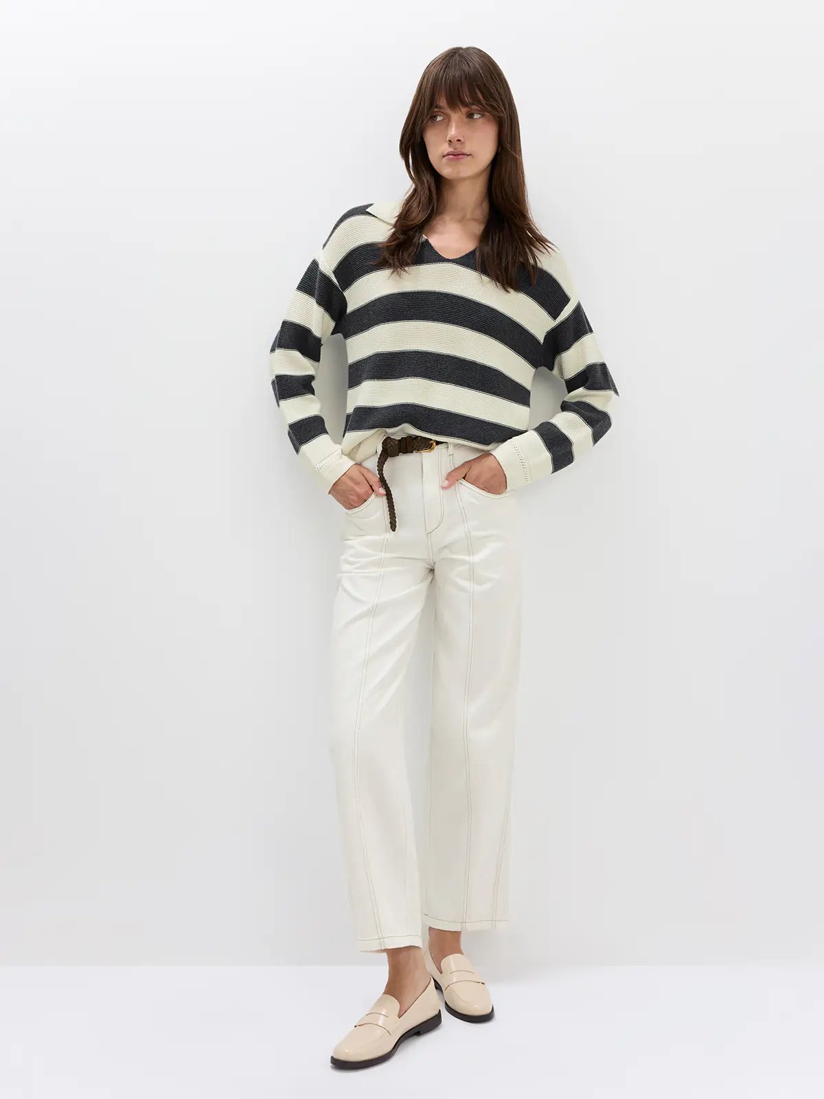 Front view of model wearing white jeans with contrast stitching, a ribbed sweater, and holding a woven bag.