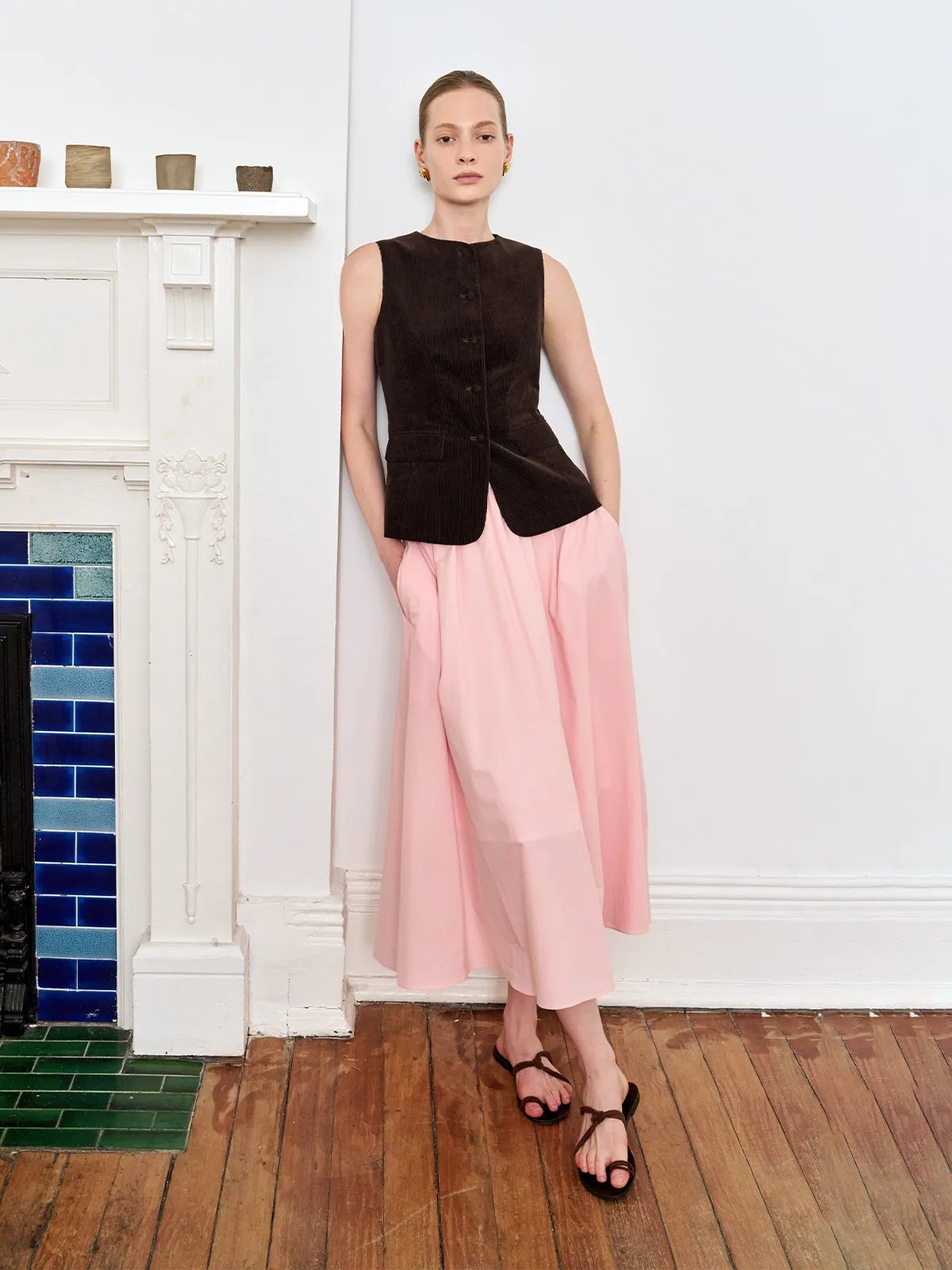 Andreatang AIDAN brown corduroy vest worn with pink midi skirt against white fireplace mantel, minimalist quiet luxury styling