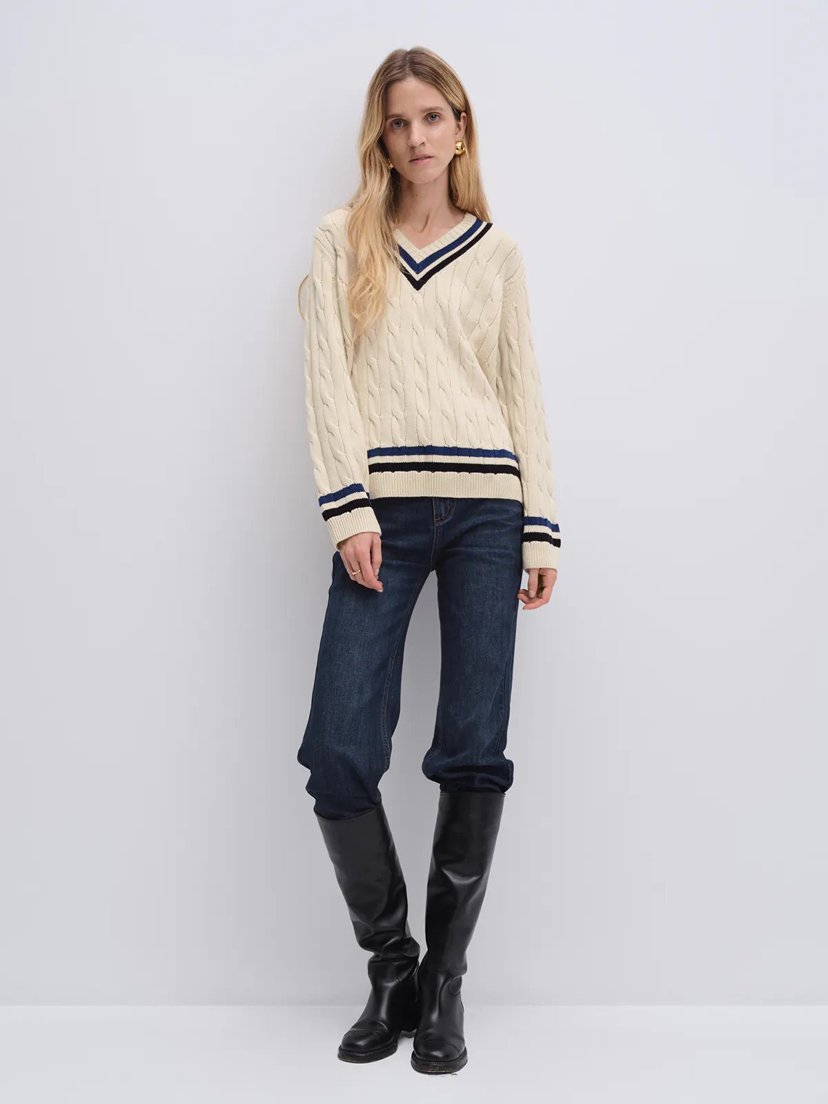 Off-white cable knit V-neck tennis jumper with contrasting trim, layered over a collared shirt and paired with a denim skirt.