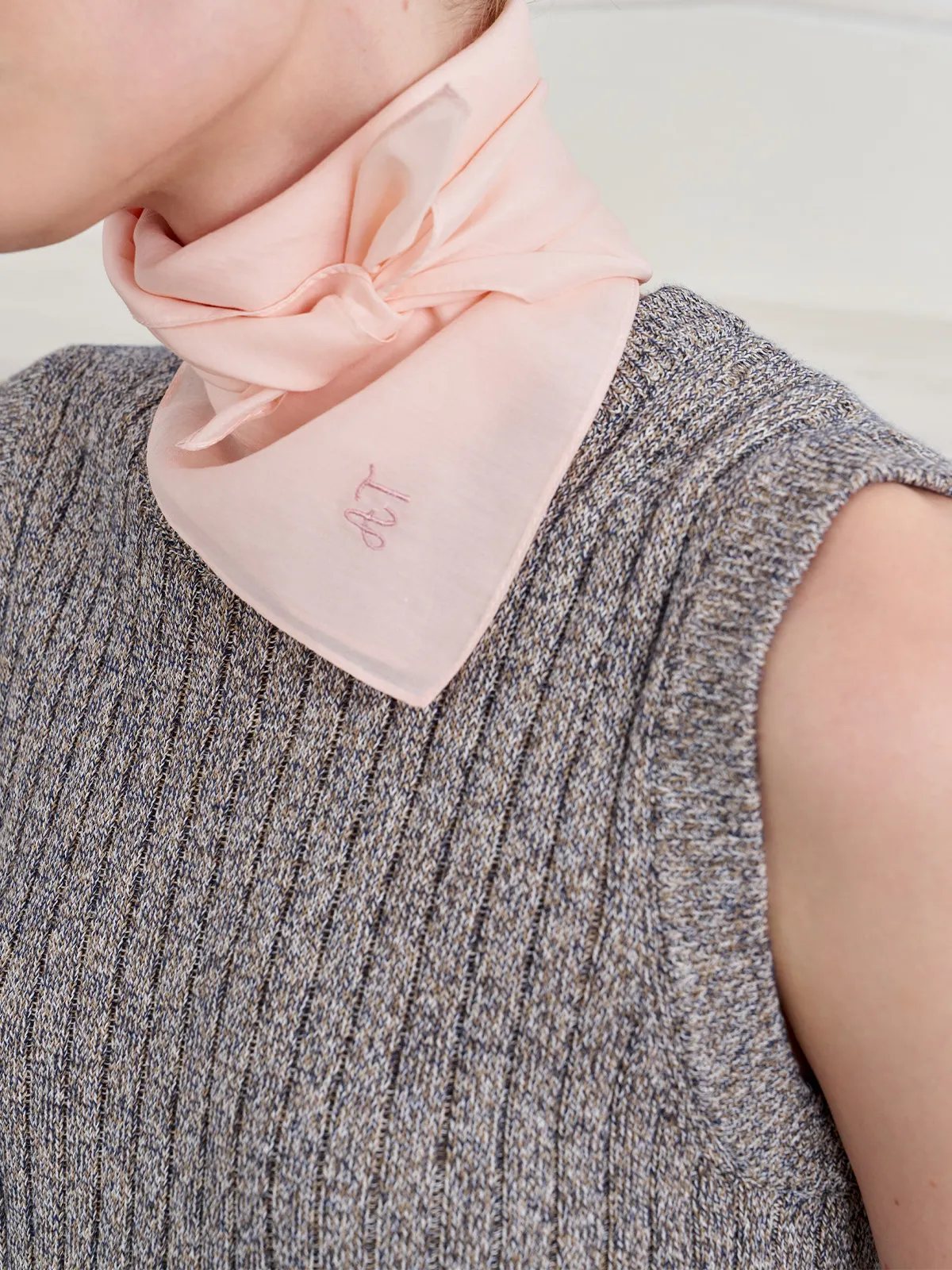 Model wearing blush pink TIANA scarf tied at neck over ribbed knit sleeveless top, monogram visible